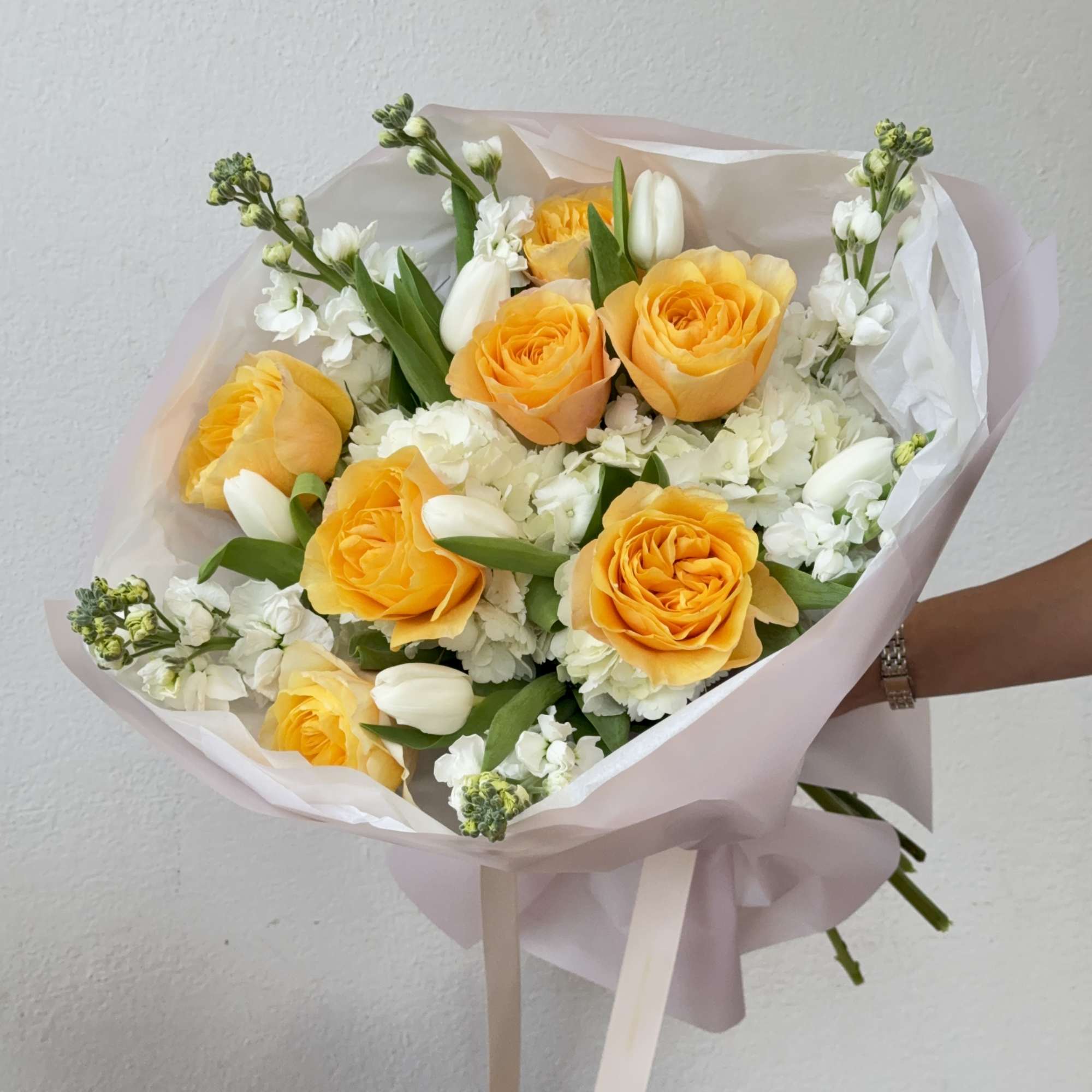 Bouquet of yellow roses and white flowers wrapped in pale pink paper