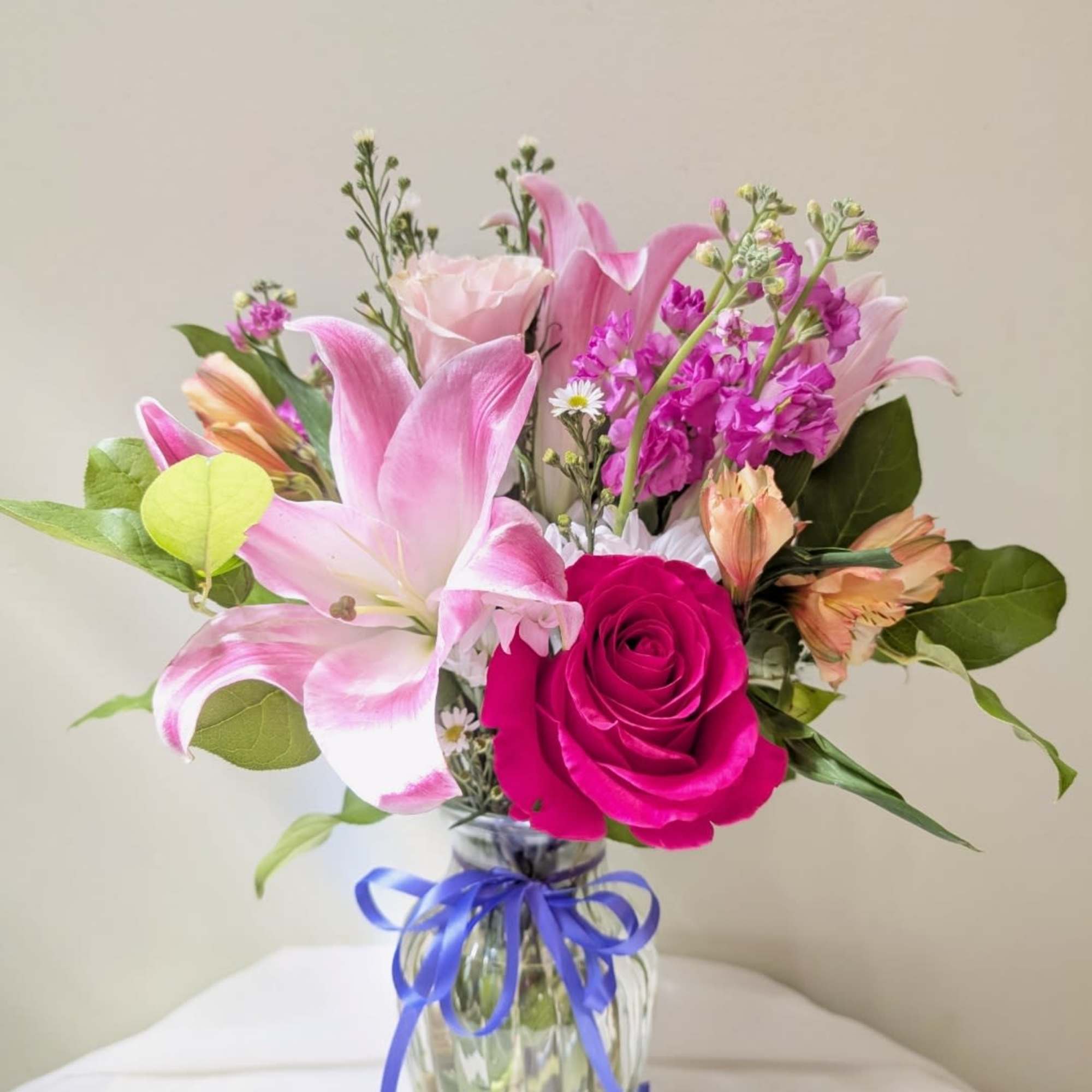 Pink lilies and a hot pink rose in a glass vase with a blue ribbon
