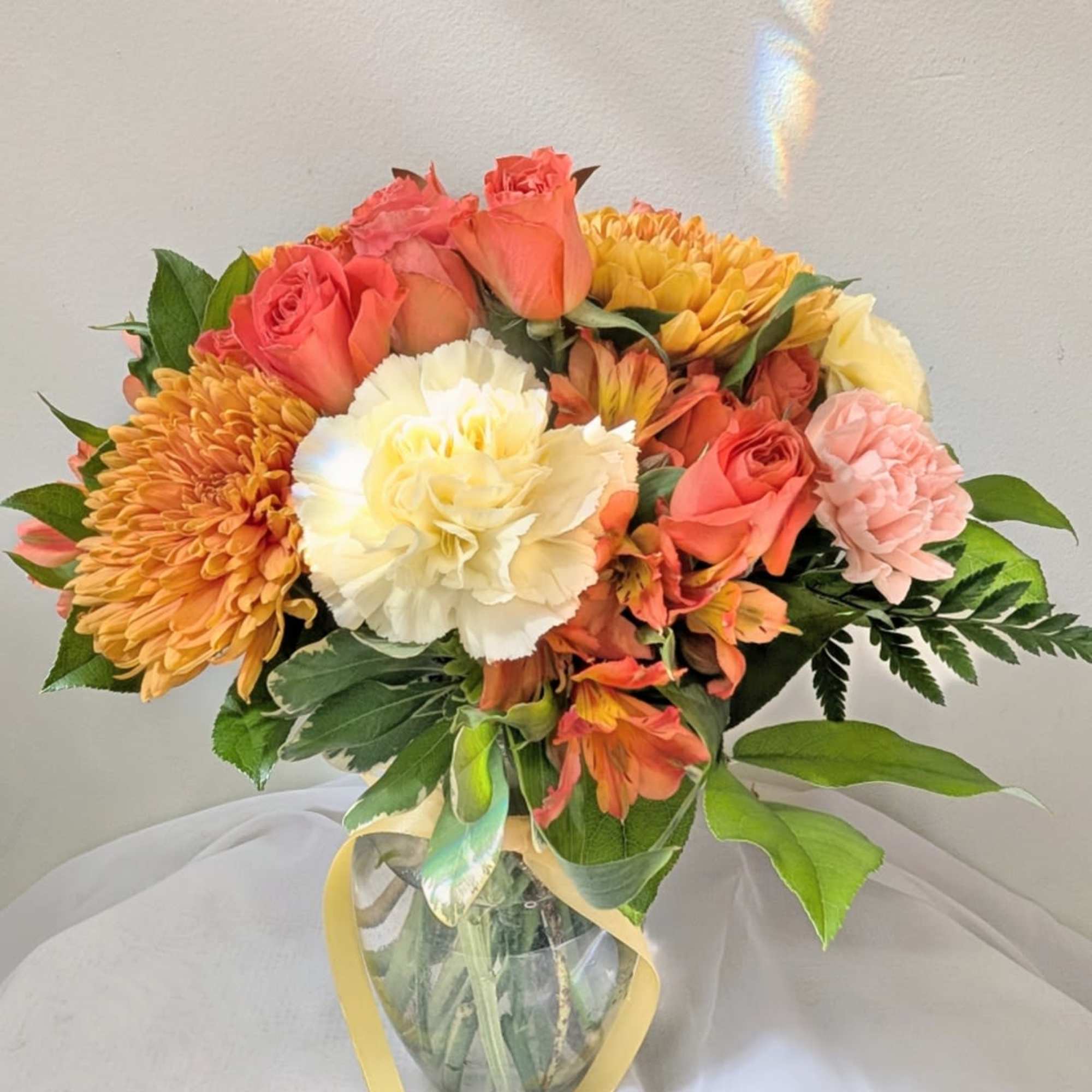Bouquet of coral roses, yellow chrysanthemums, and white carnations in a glass vase