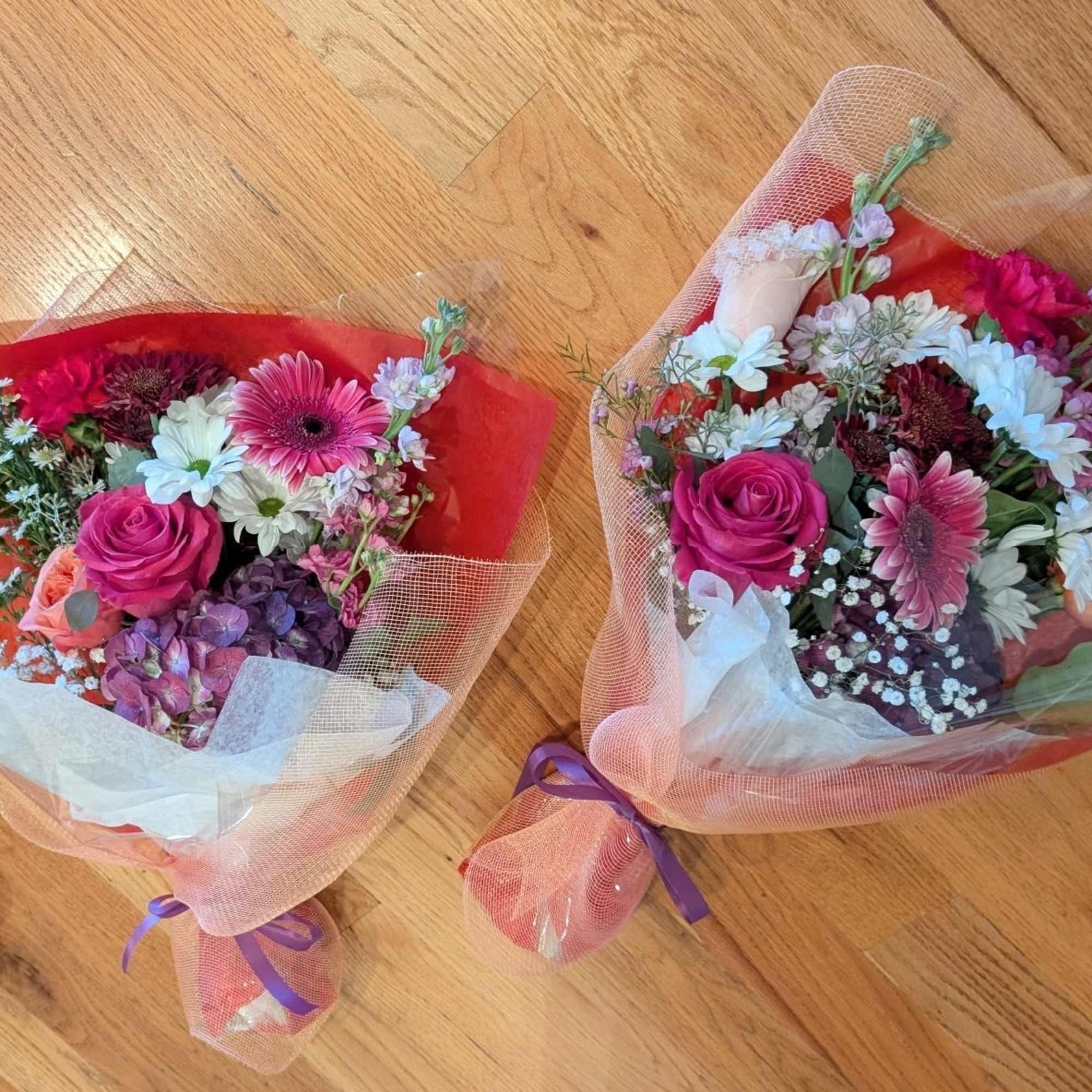 Two mixed flower bouquets wrapped in pink mesh and red paper on a wooden floor