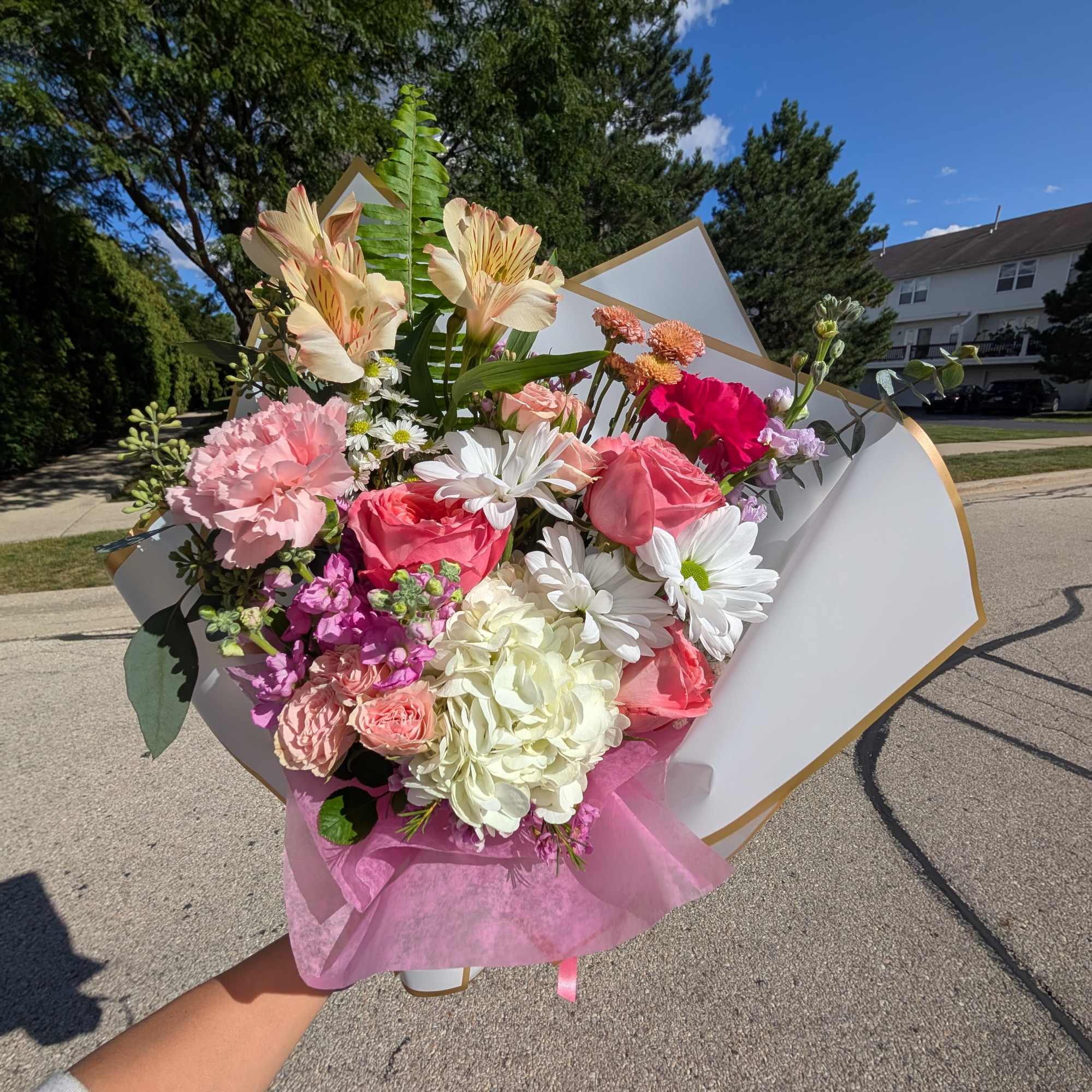 Handheld bouquet of pink, white, and peach flowers wrapped in white paper