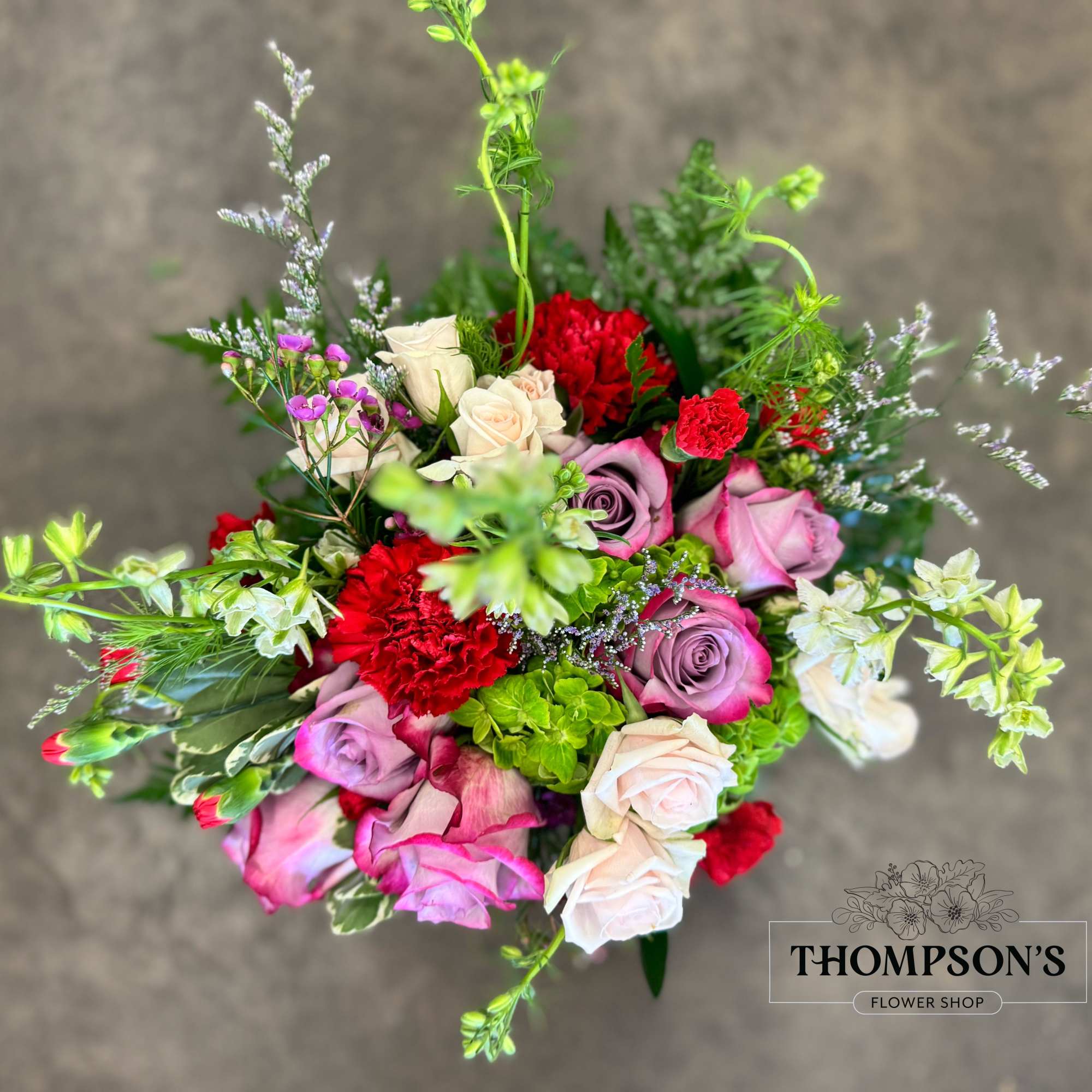 A lush blend of lavender roses, rich red carnations, green hydrangea, blush