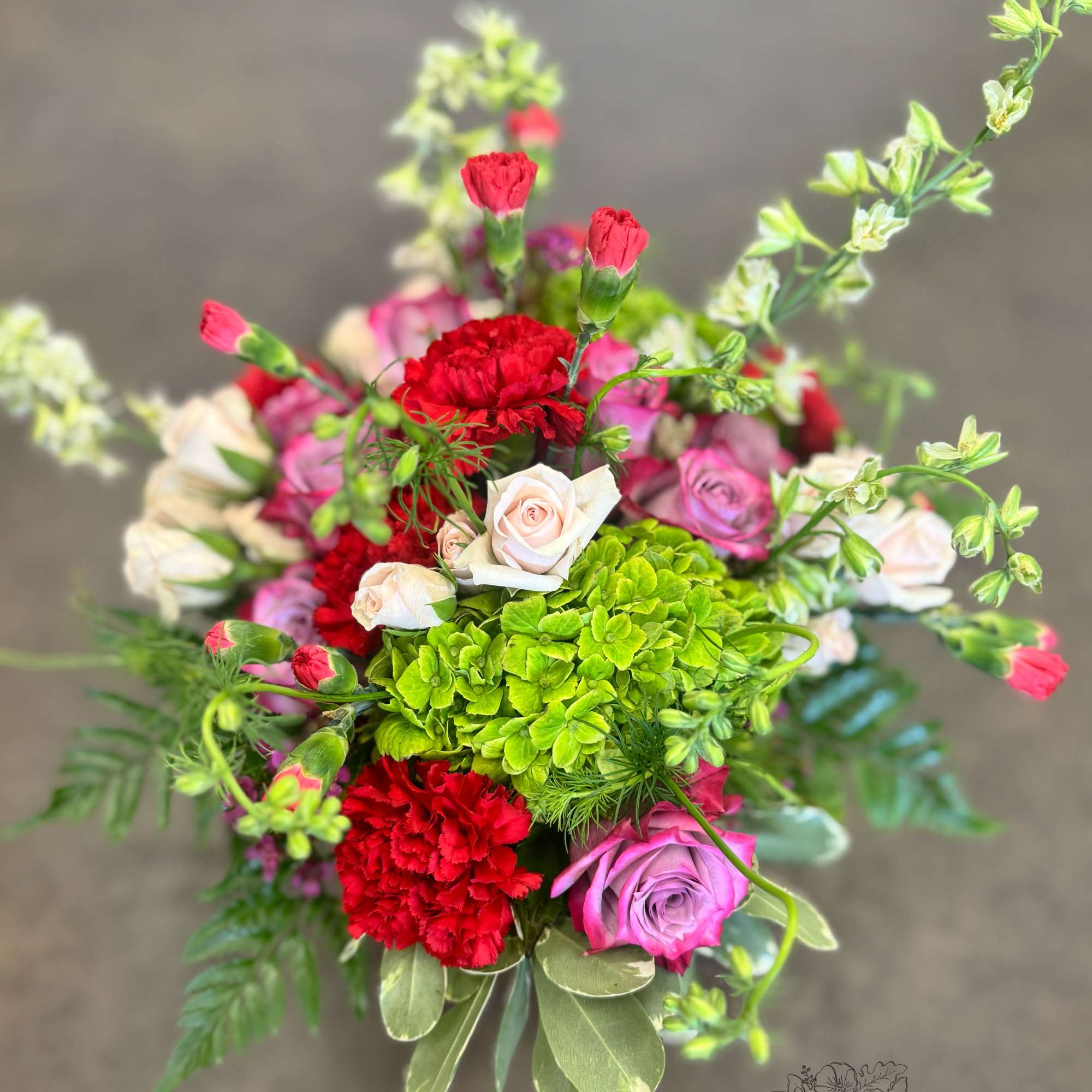 A lush blend of lavender roses, rich red carnations, green hydrangea, blush