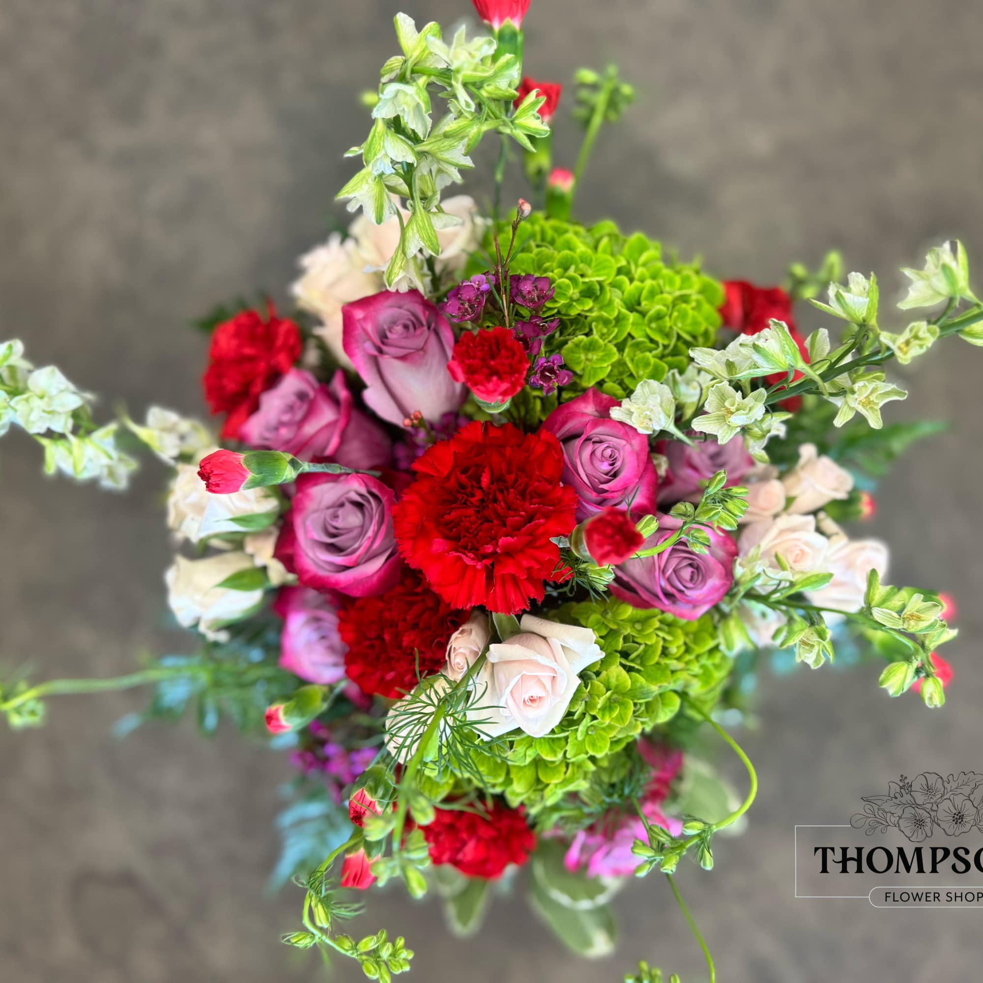 A lush blend of lavender roses, rich red carnations, green hydrangea, blush
