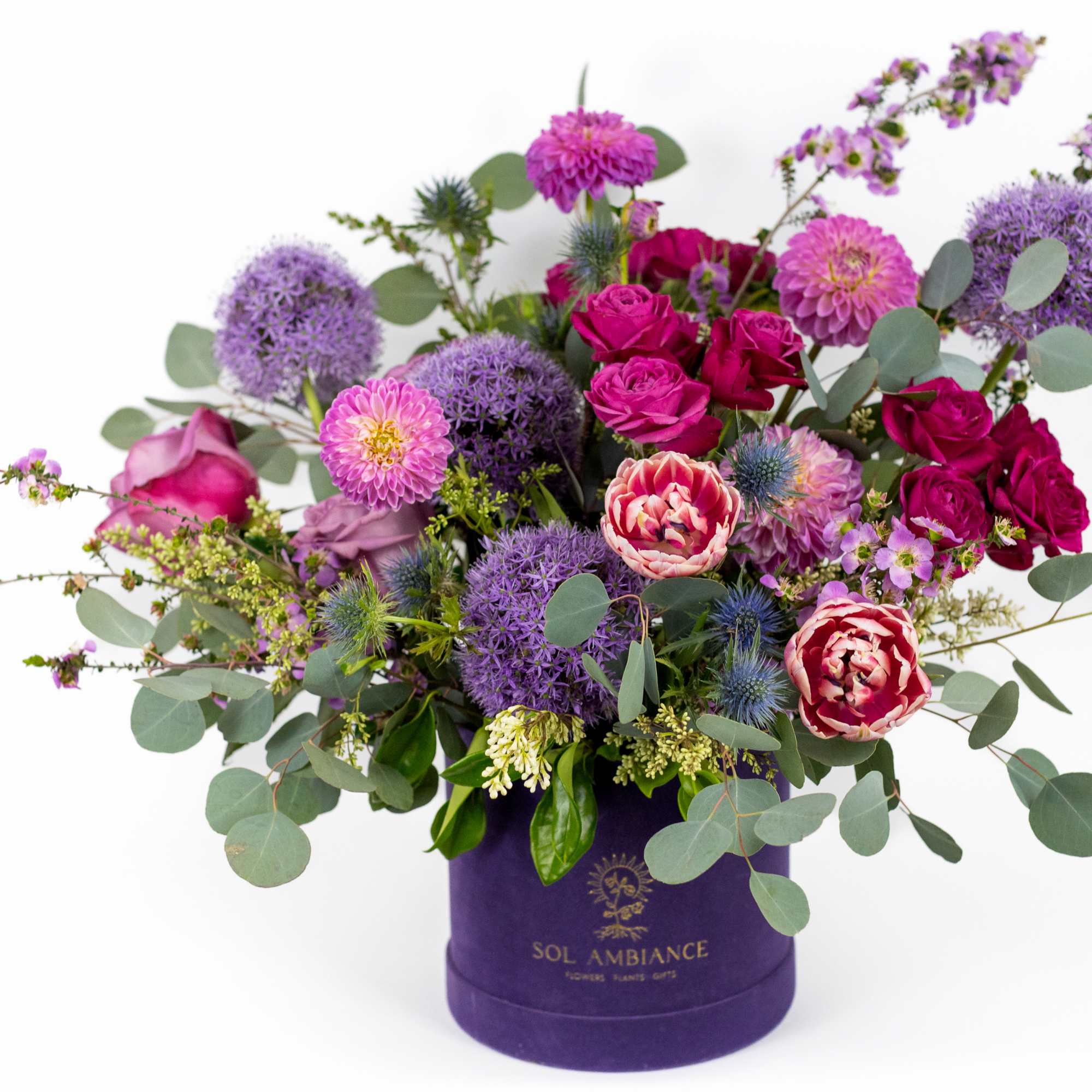 Purple and pink mixed flower arrangement in a purple hatbox