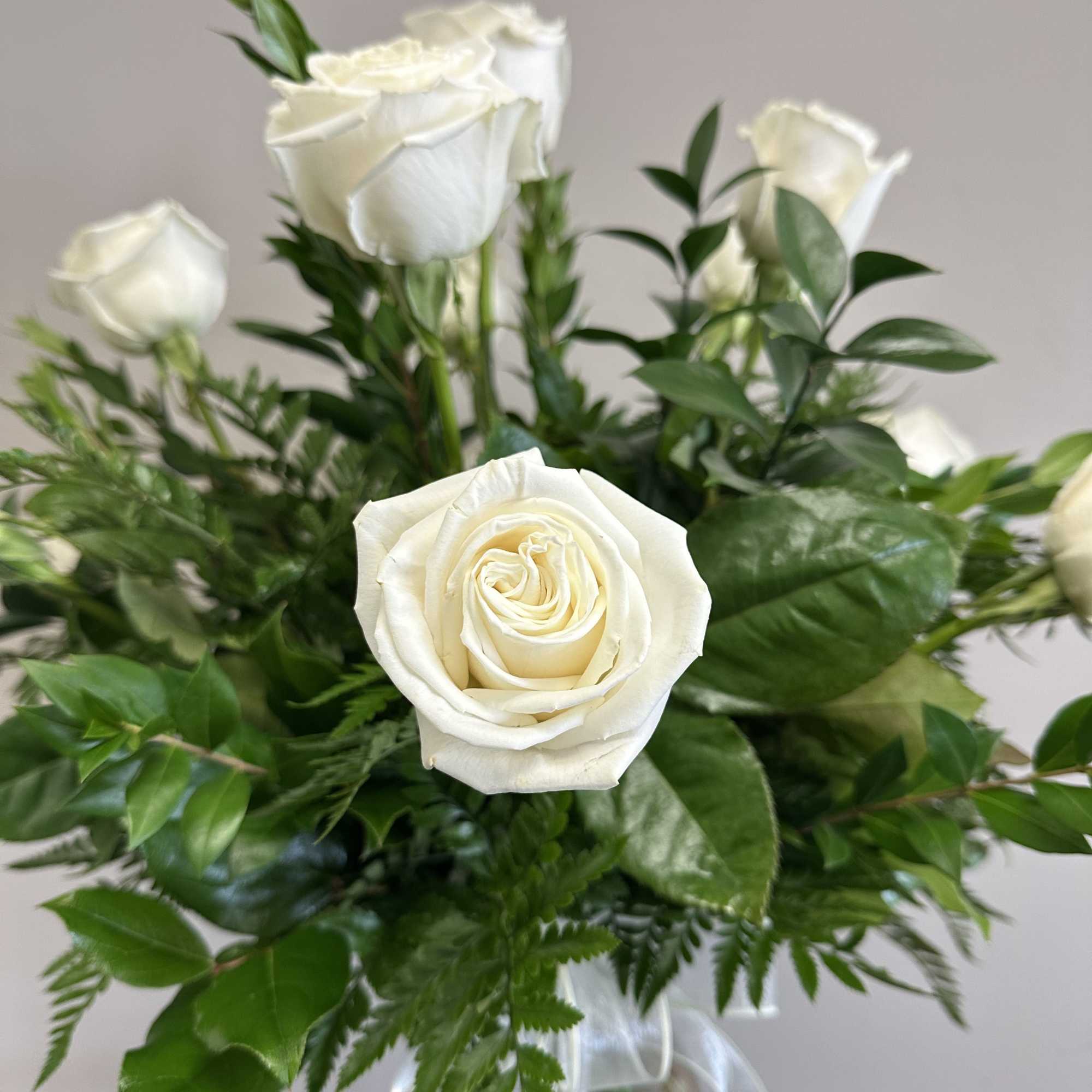 A dozen long stem white roses with assorted greenery in a clear