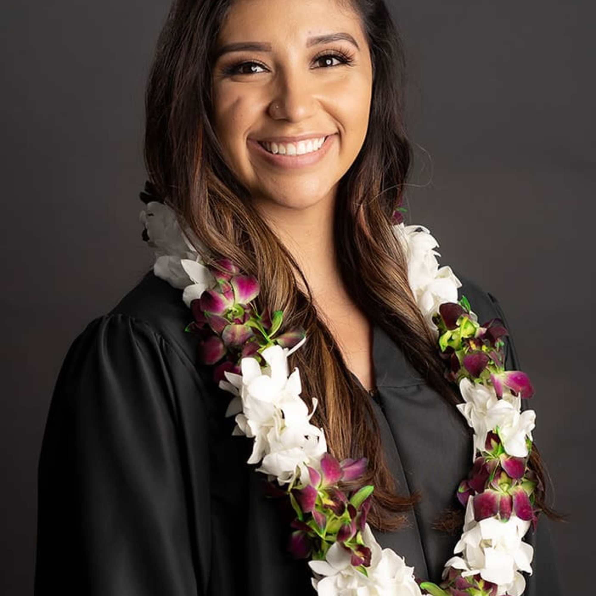 Woman wearing a white and purple orchid lei over a black graduation gown