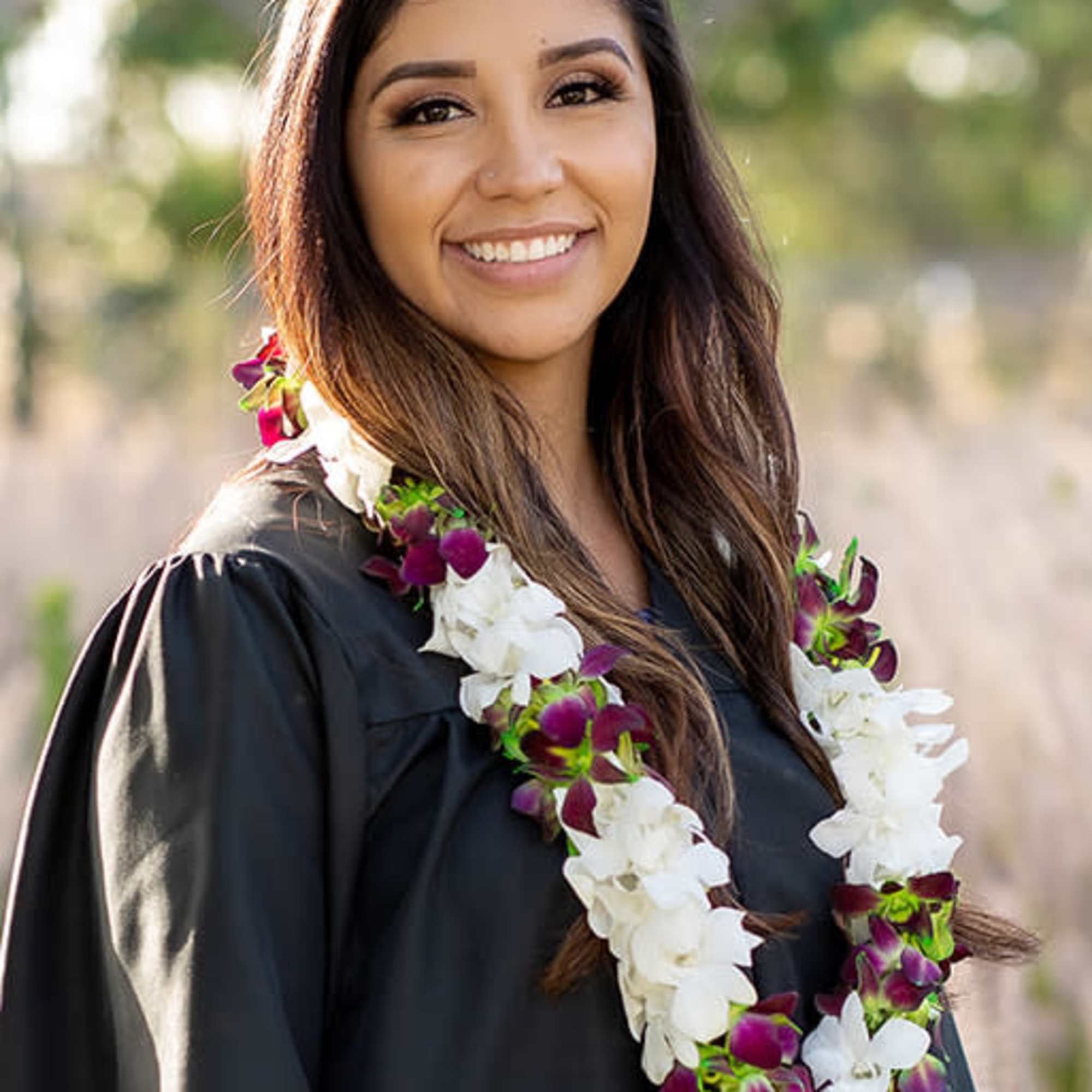 Woman wearing a white and purple flower lei over a black graduation gown