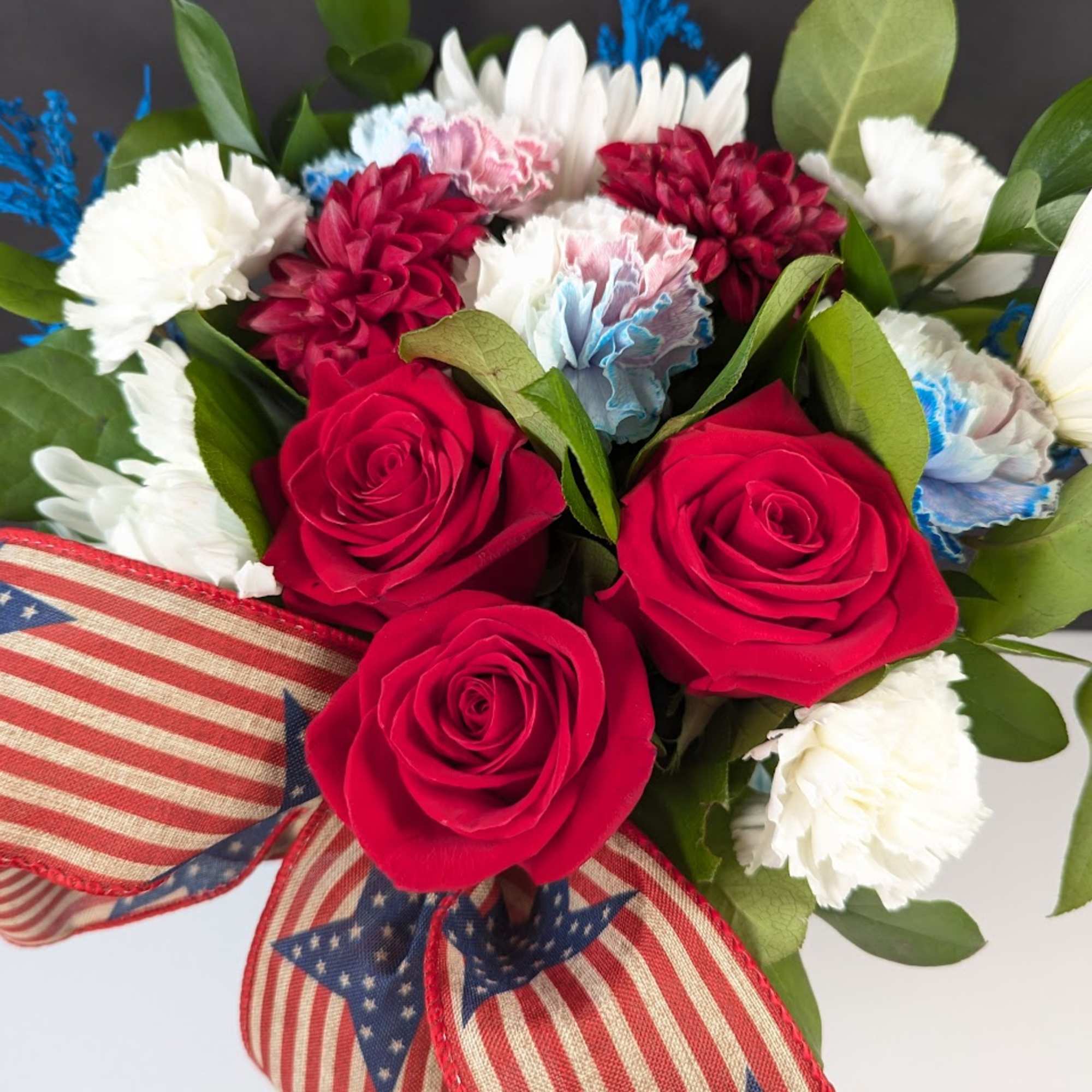 Bouquet of red roses, white carnations, and blue accents with an American flag ribbon