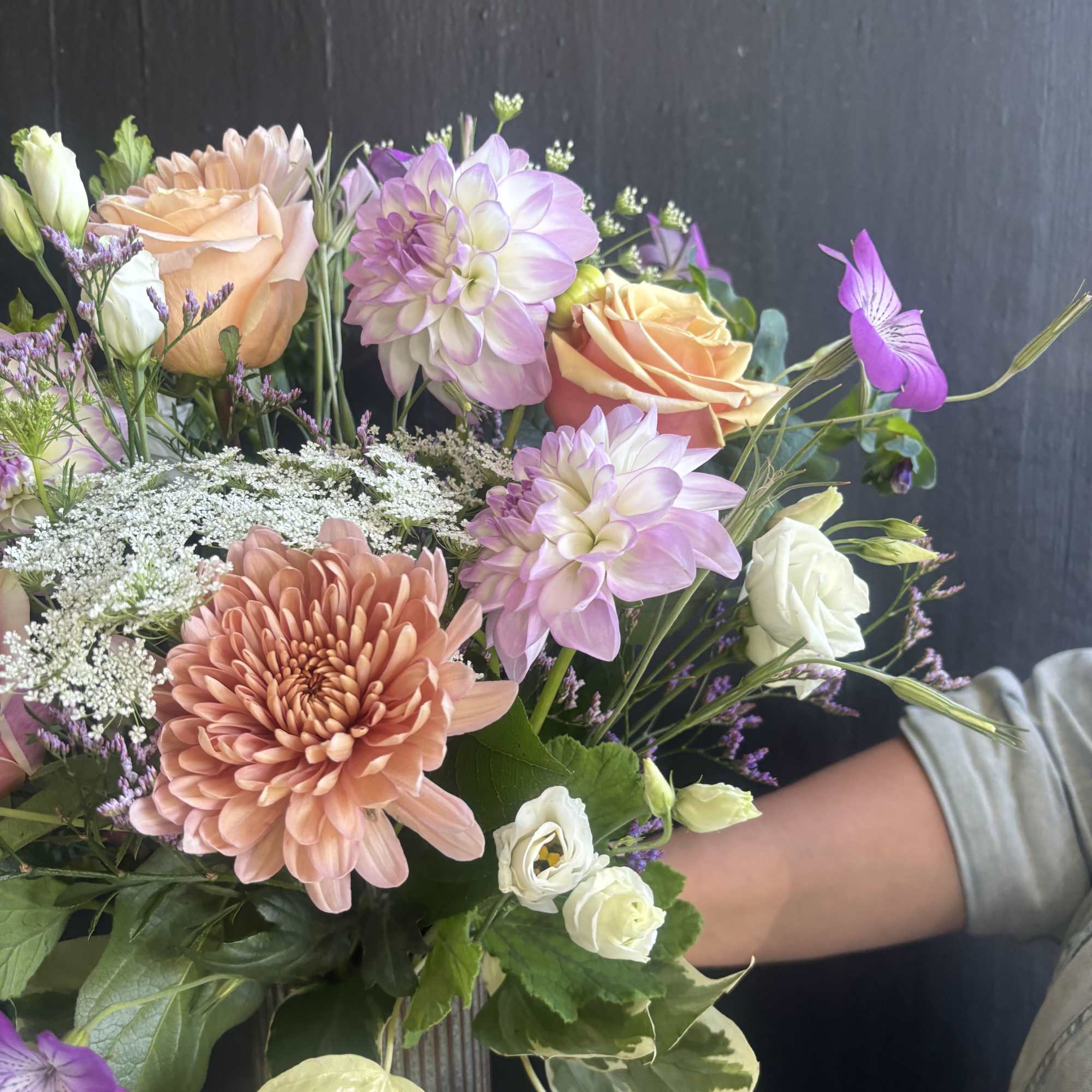 This weekly seasonal arrangement showcases lavender dahlias, peach roses, and Queen Anne's