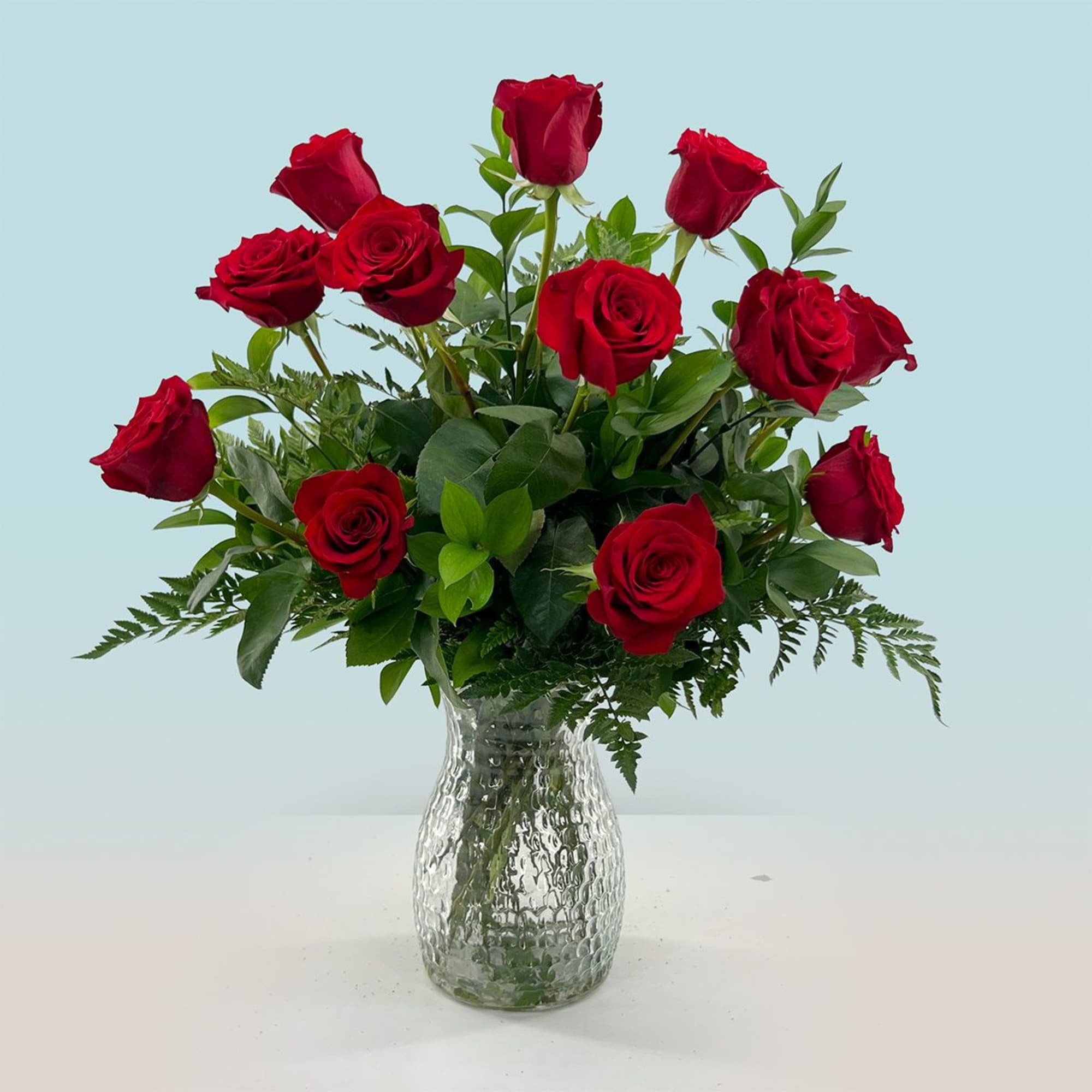 A dozen long-stemmed red roses gathered in a clear, textured glass vase