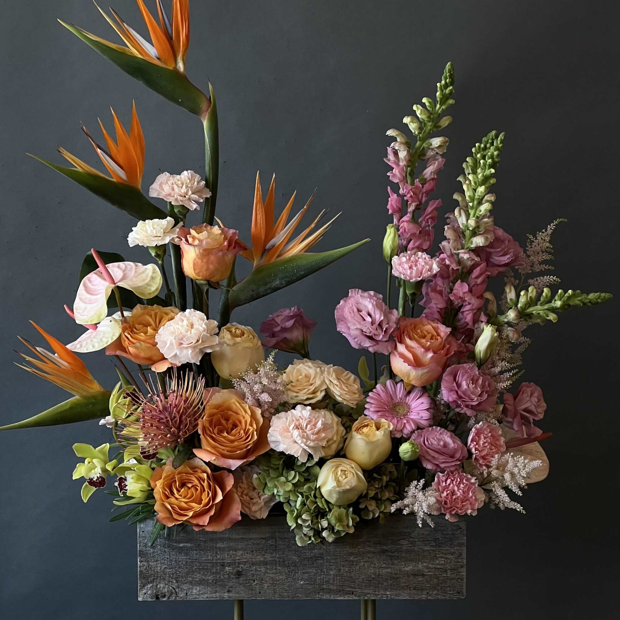 Tall floral arrangement with orange birds of paradise and pink roses in a wooden container