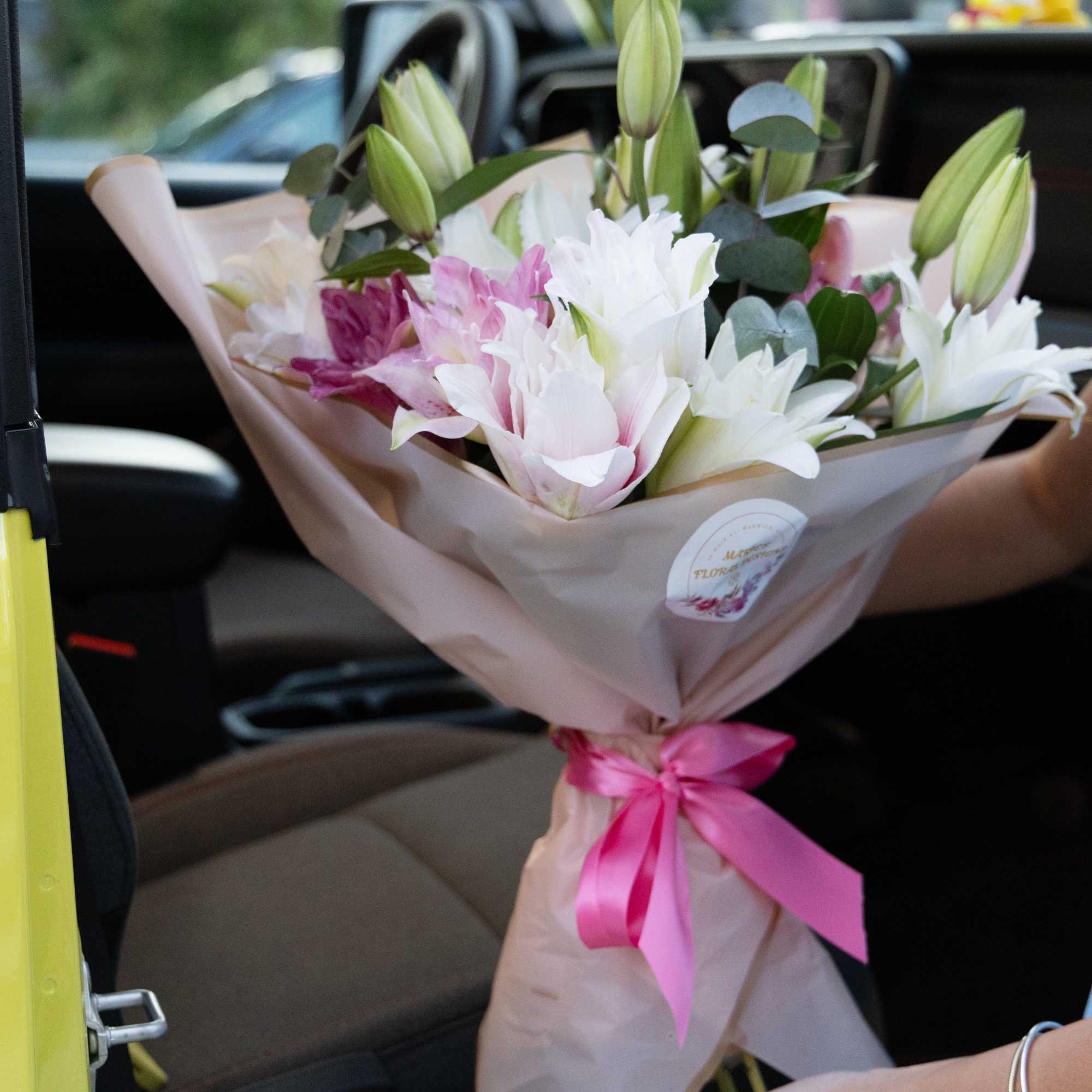 Bouquet of pink and white lilies wrapped in paper with a pink ribbon