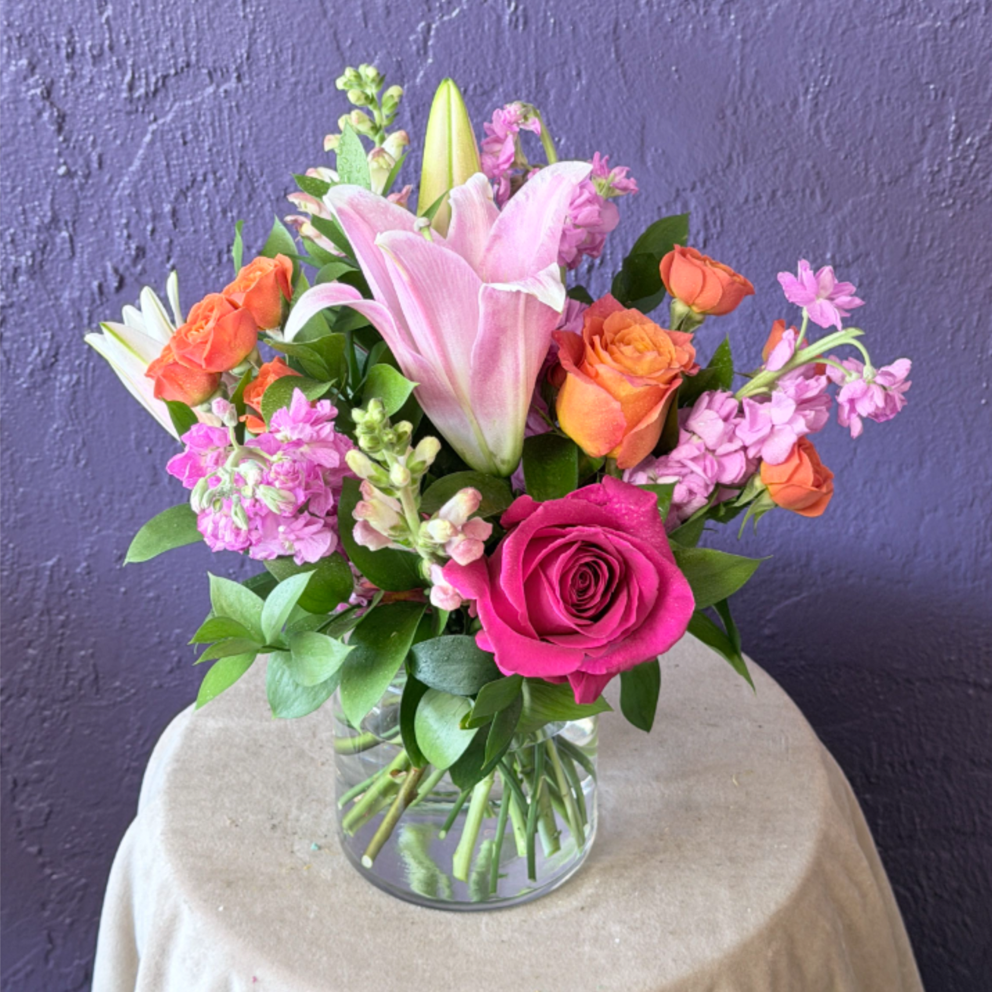 Pink lilies and roses arranged in a clear glass vase