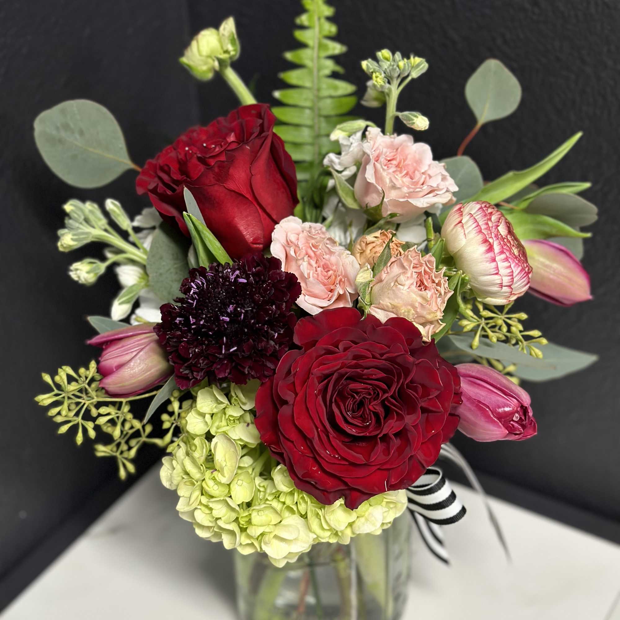 Bouquet of red roses, pink tulips, and pale hydrangea in a glass vase