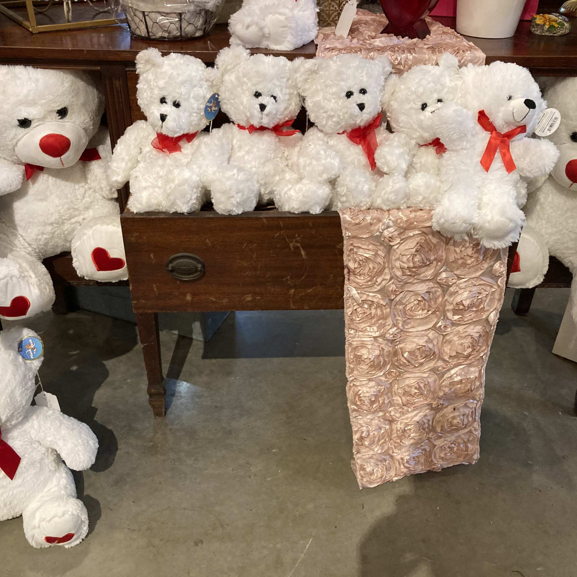 White teddy bears with red bows arranged around a pink rose-covered gift box.
