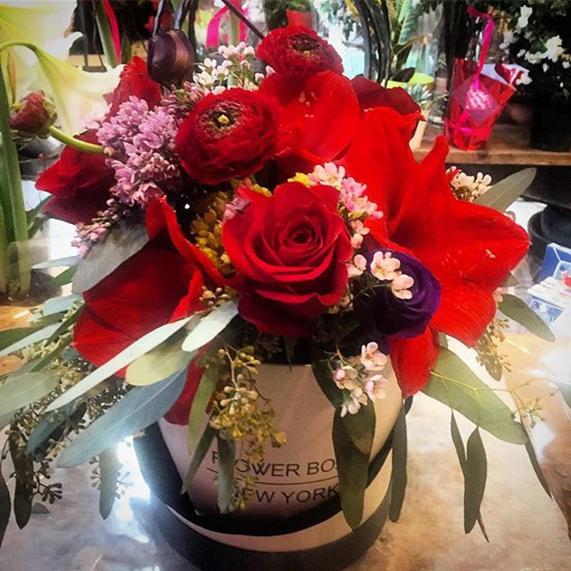 Red roses and mixed blooms arranged in a hatbox-style container