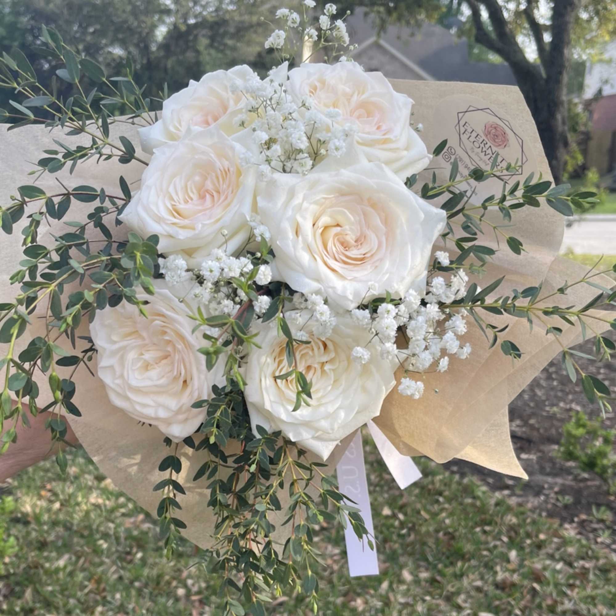 Bouquet of white roses with baby's breath and greenery in kraft paper
