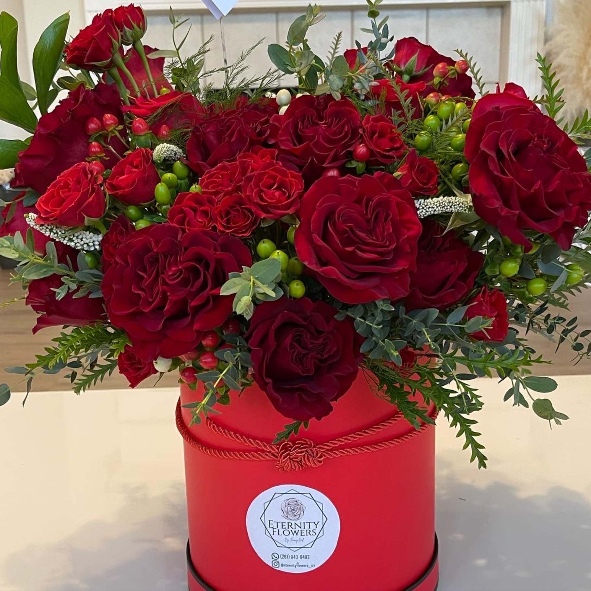 Red roses arranged in a red hatbox with greenery