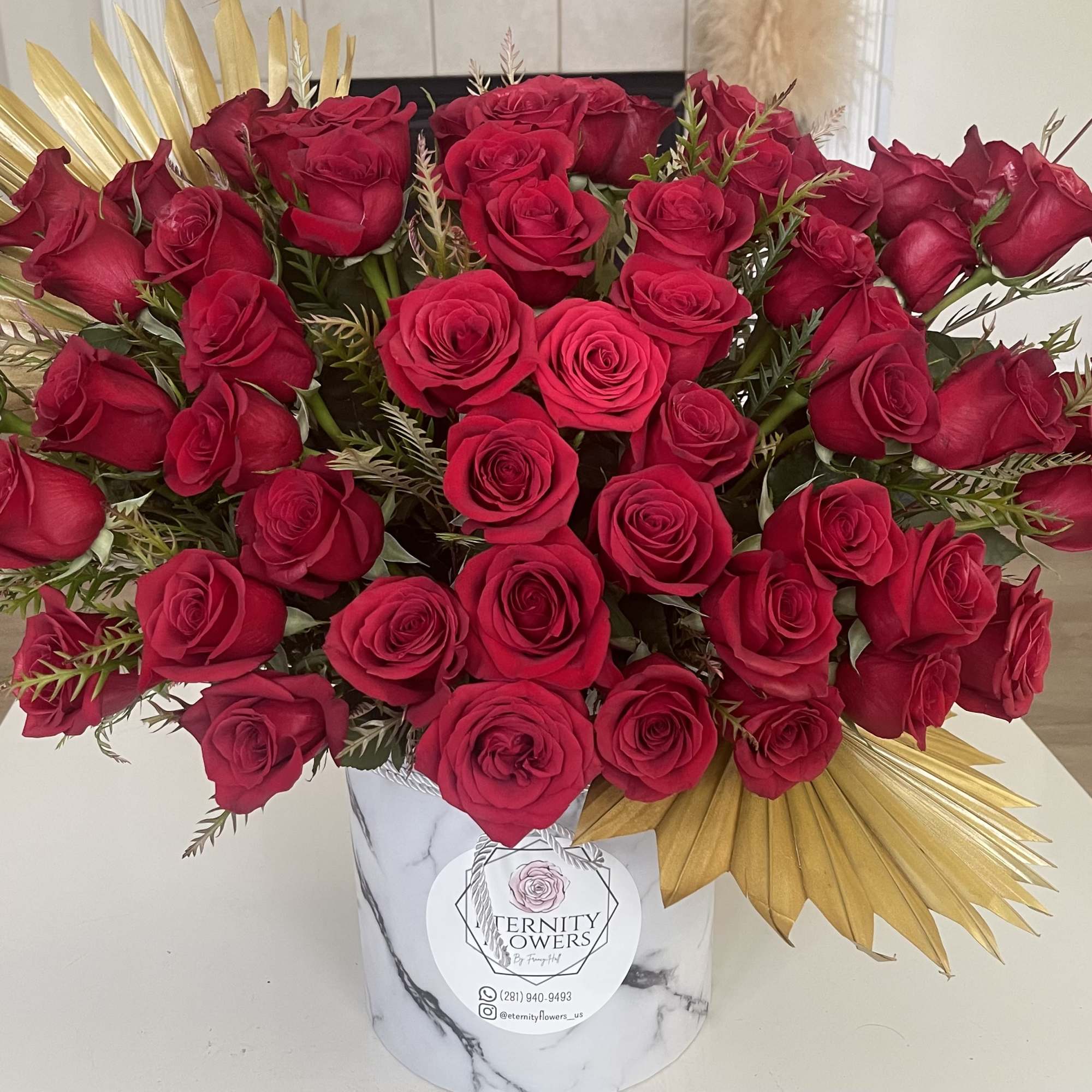 Large bouquet of red roses in a white marble-patterned box with gold accents.