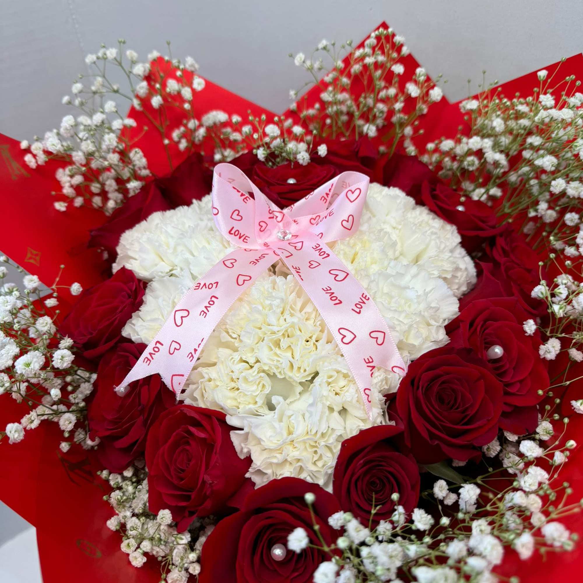 Red roses and white carnations with baby's breath, tied with a pink ribbon