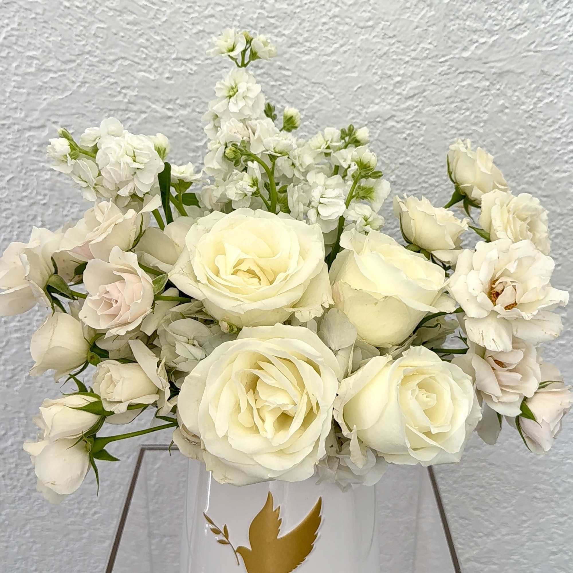 An elegant collection of ivory roses, blush spray roses, and white stock