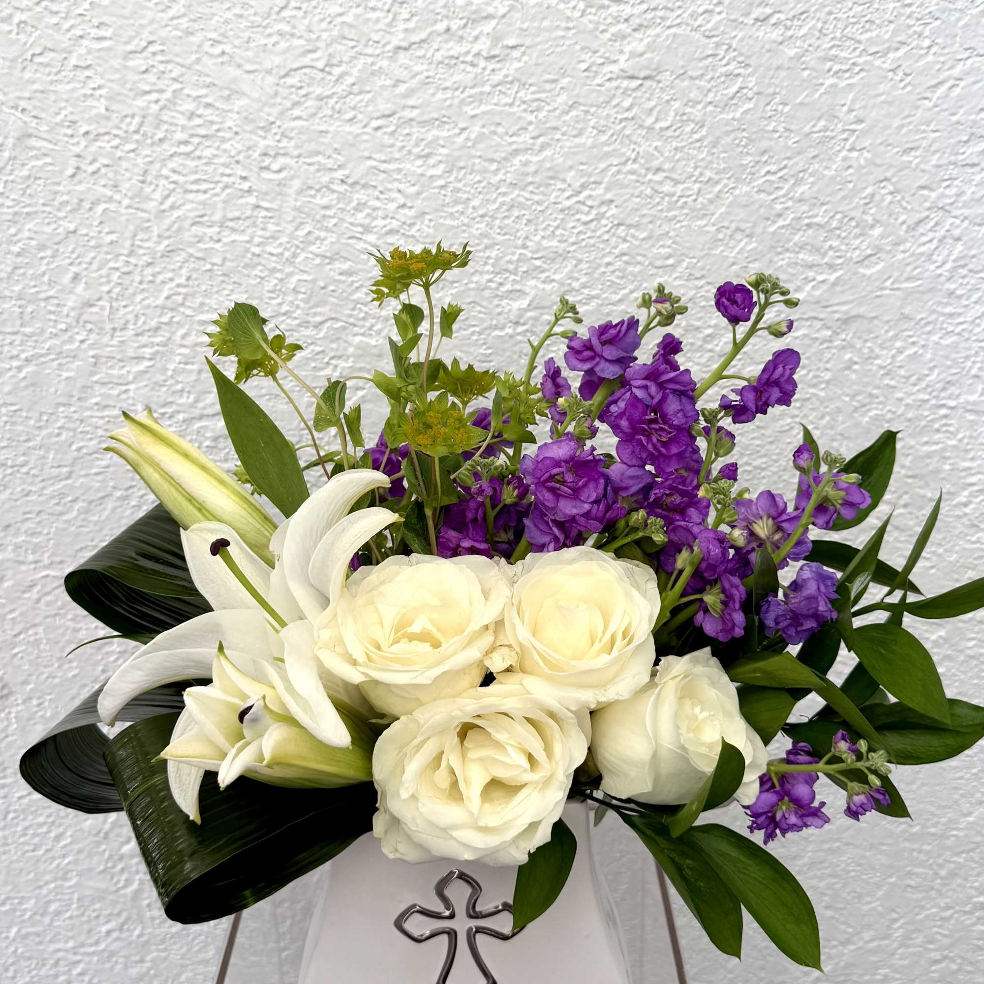 Designed with graceful white lilies, creamy ivory roses,  and rich purple