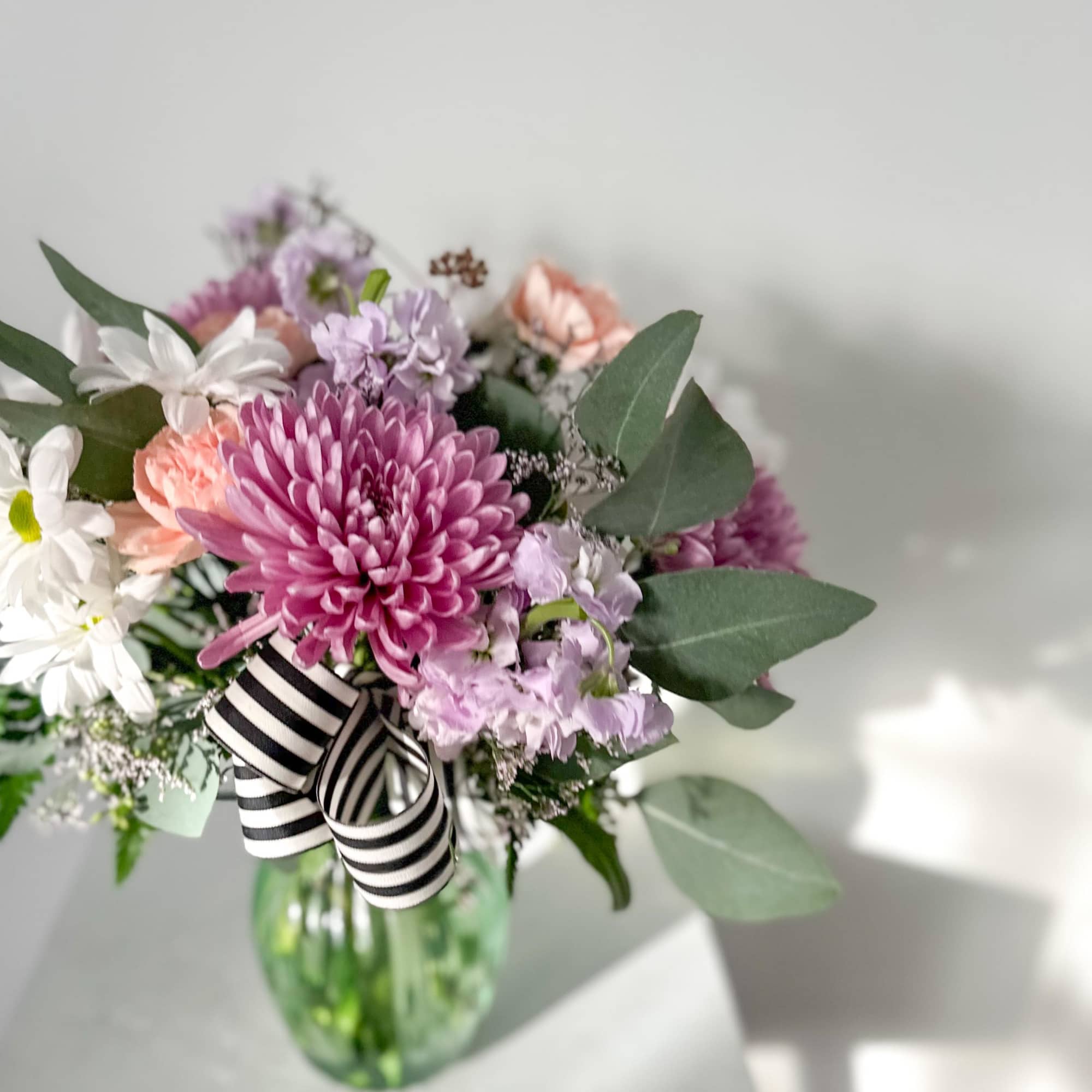Pink and lavender bouquet in a glass vase with a striped ribbon