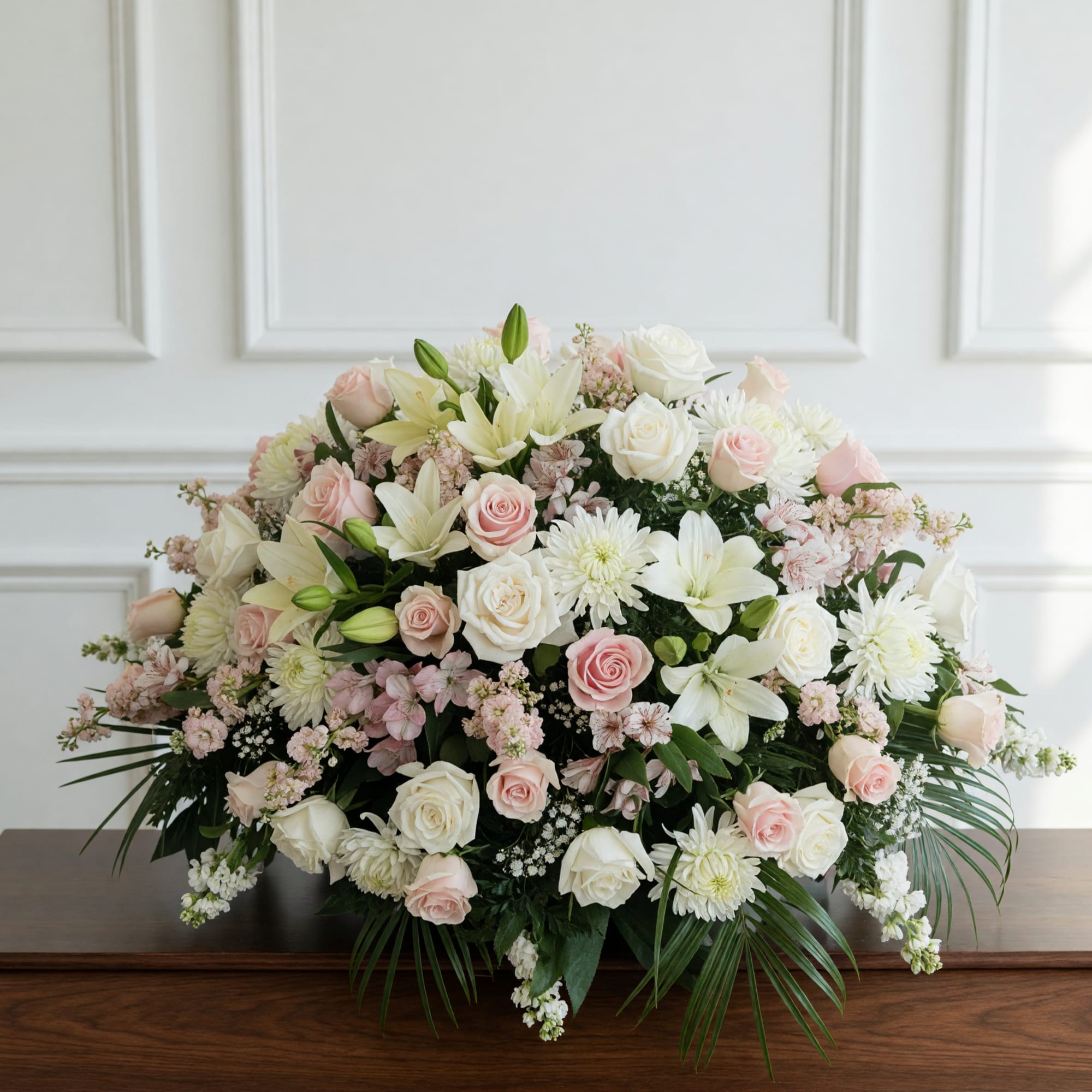 A softly layered casket spray in white, blush pink and pale green