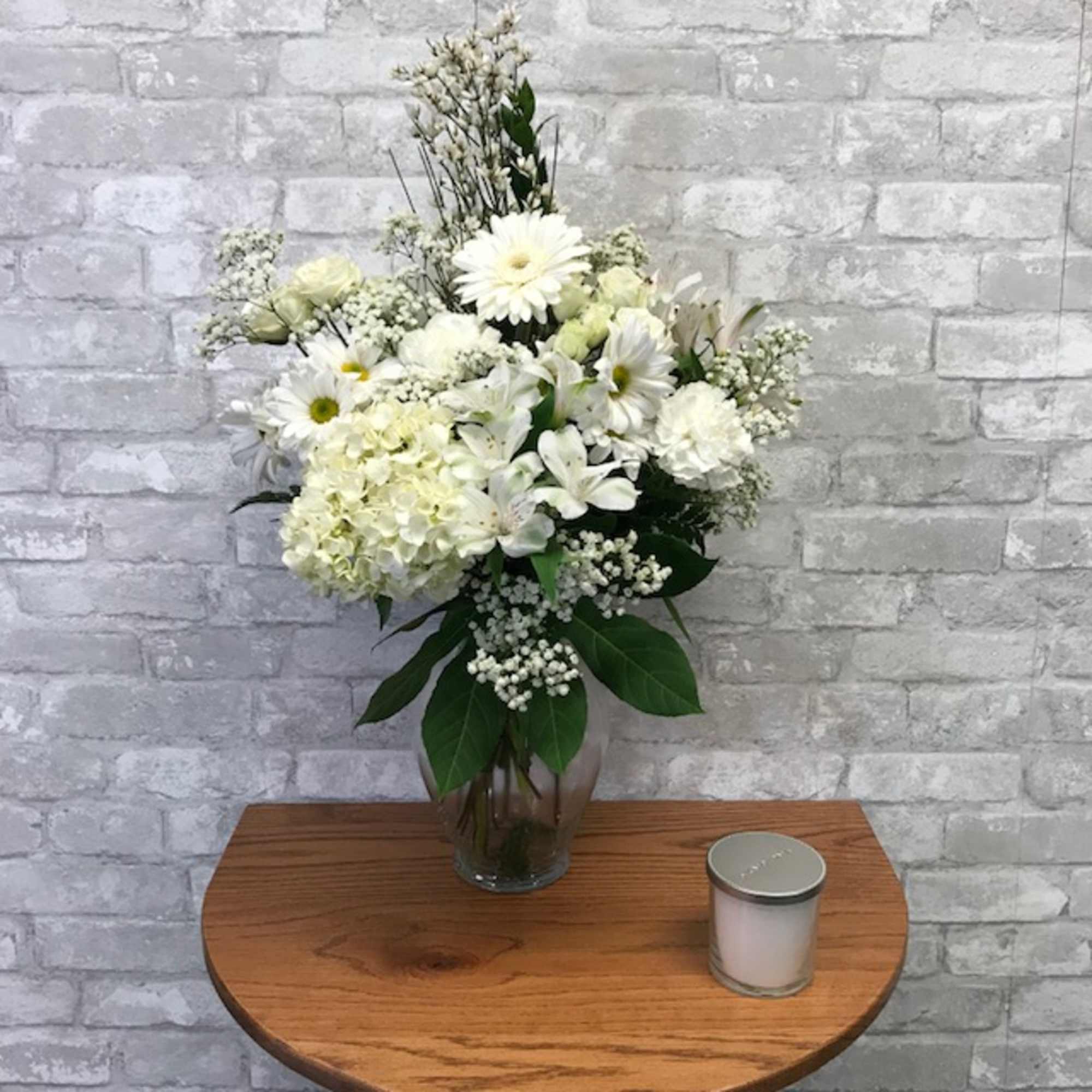 White floral arrangement in a glass vase with a candle beside it
