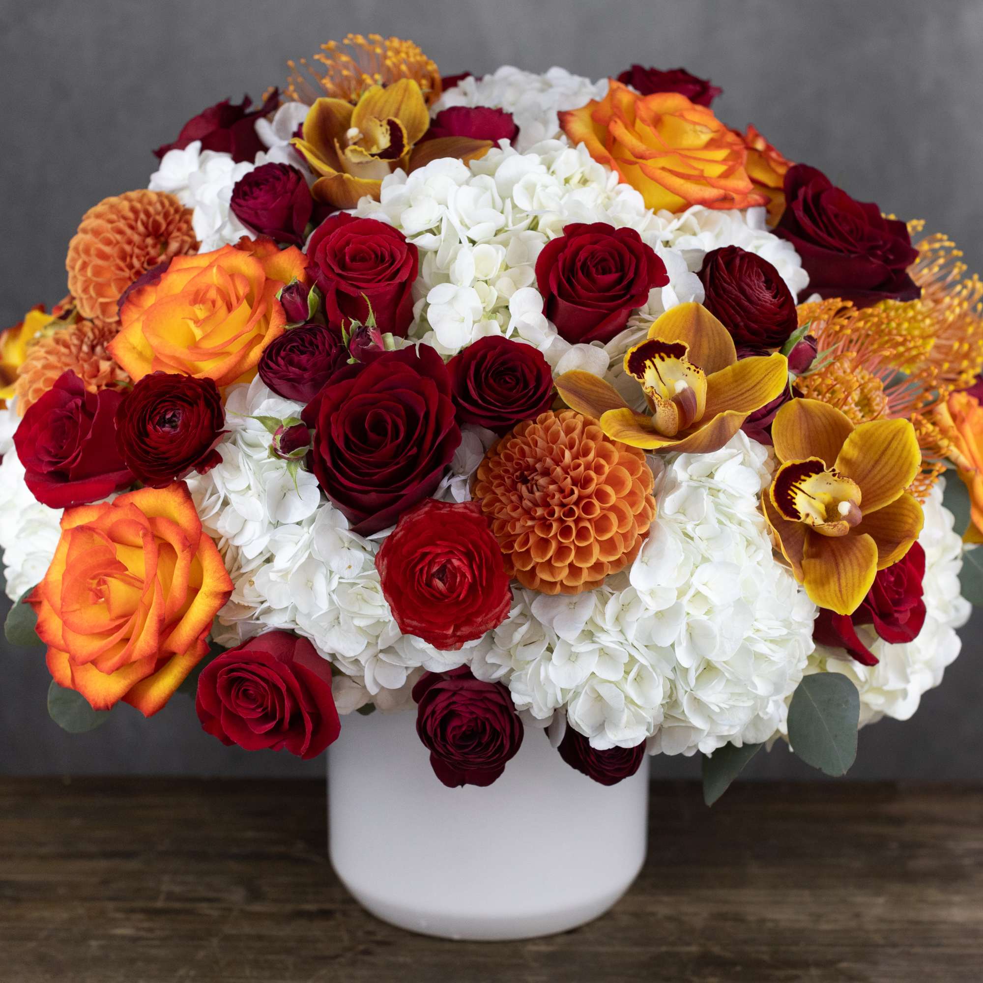 Bouquet of red and orange roses with white hydrangeas in a white vase