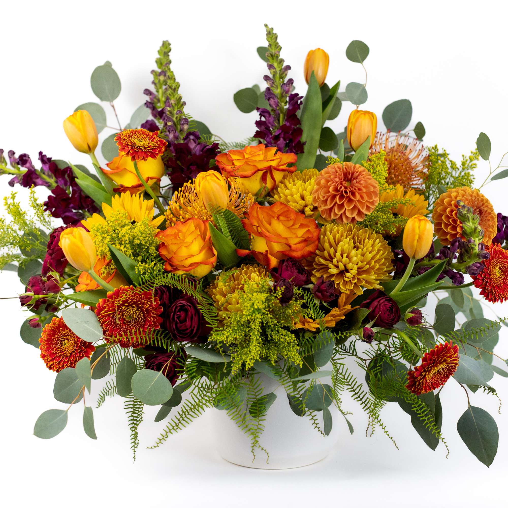 Mixed bouquet of orange, yellow, and burgundy flowers in a white vase