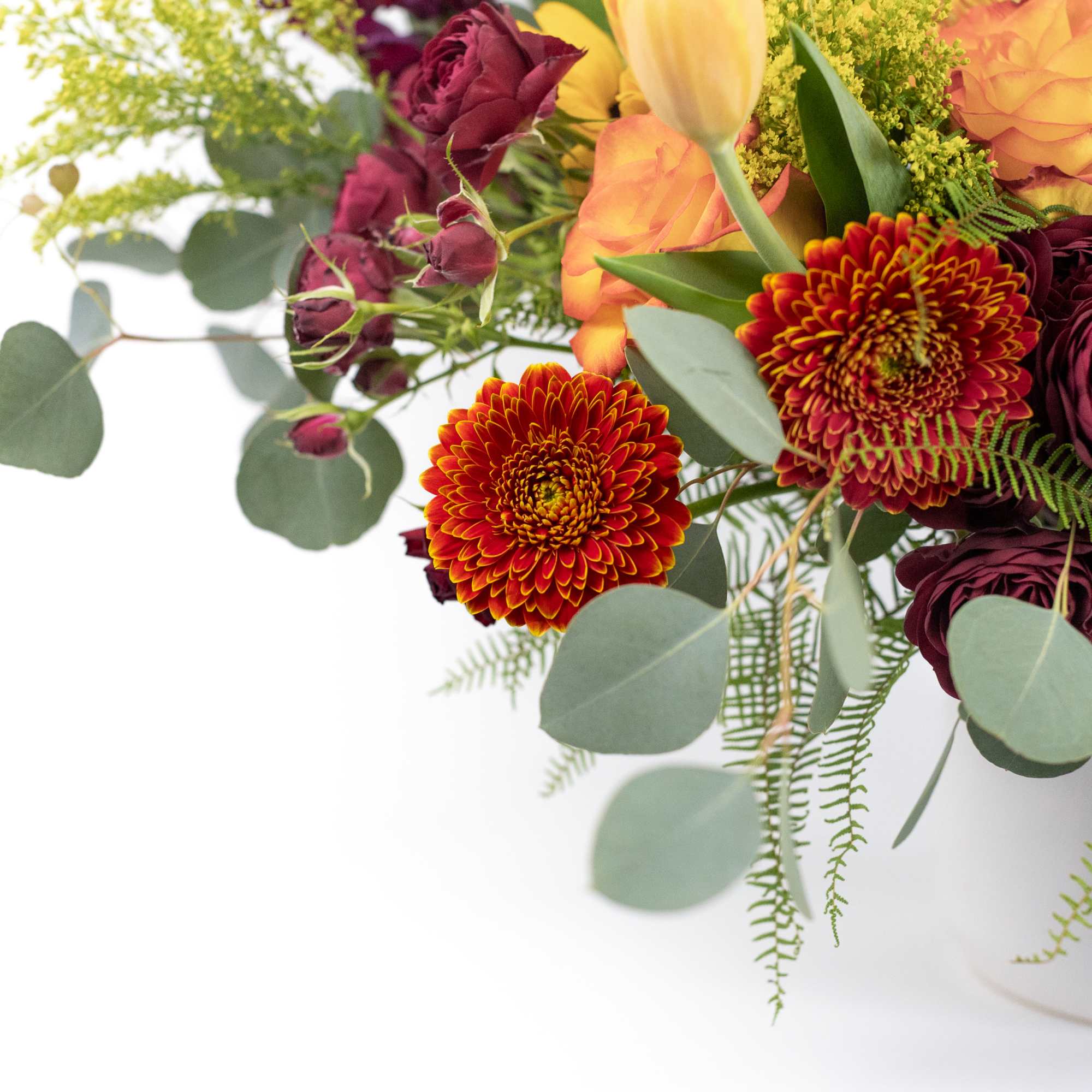 Mixed bouquet with orange roses, burgundy blooms, and chrysanthemums in a white vase
