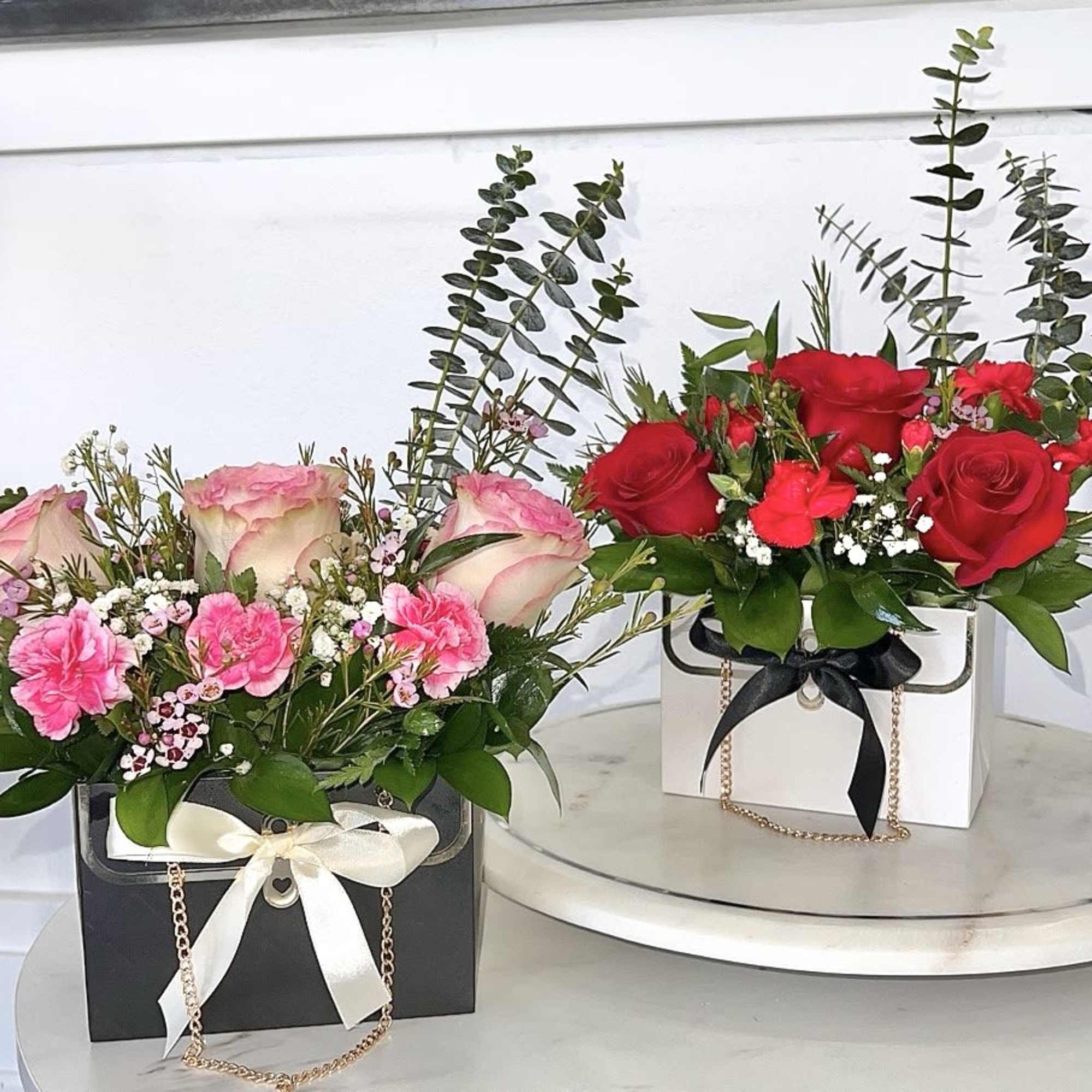 Two rose arrangements in gift boxes, one pink and one red