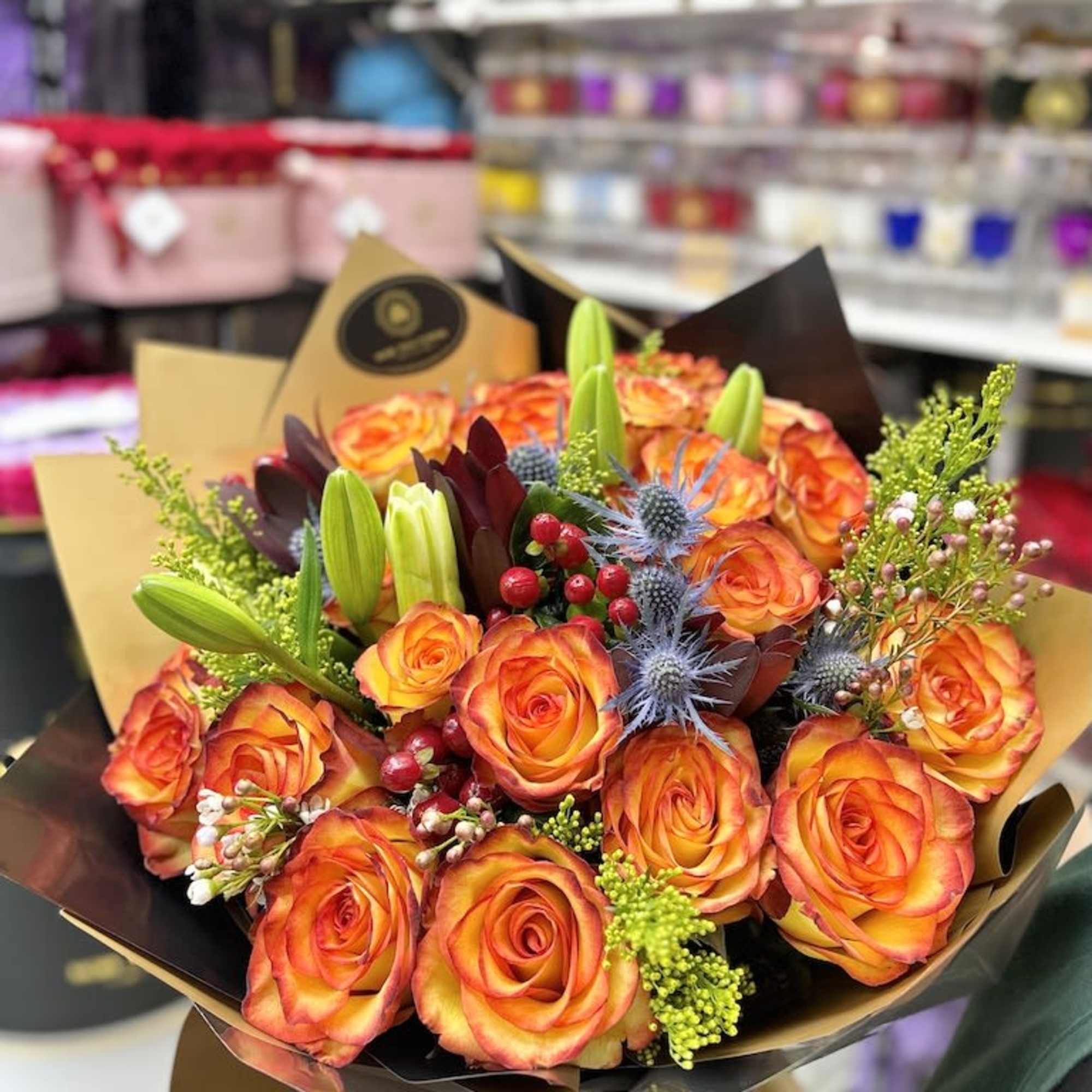 Hand-tied bouquet of orange roses with lilies and accent flowers in decorative wrap