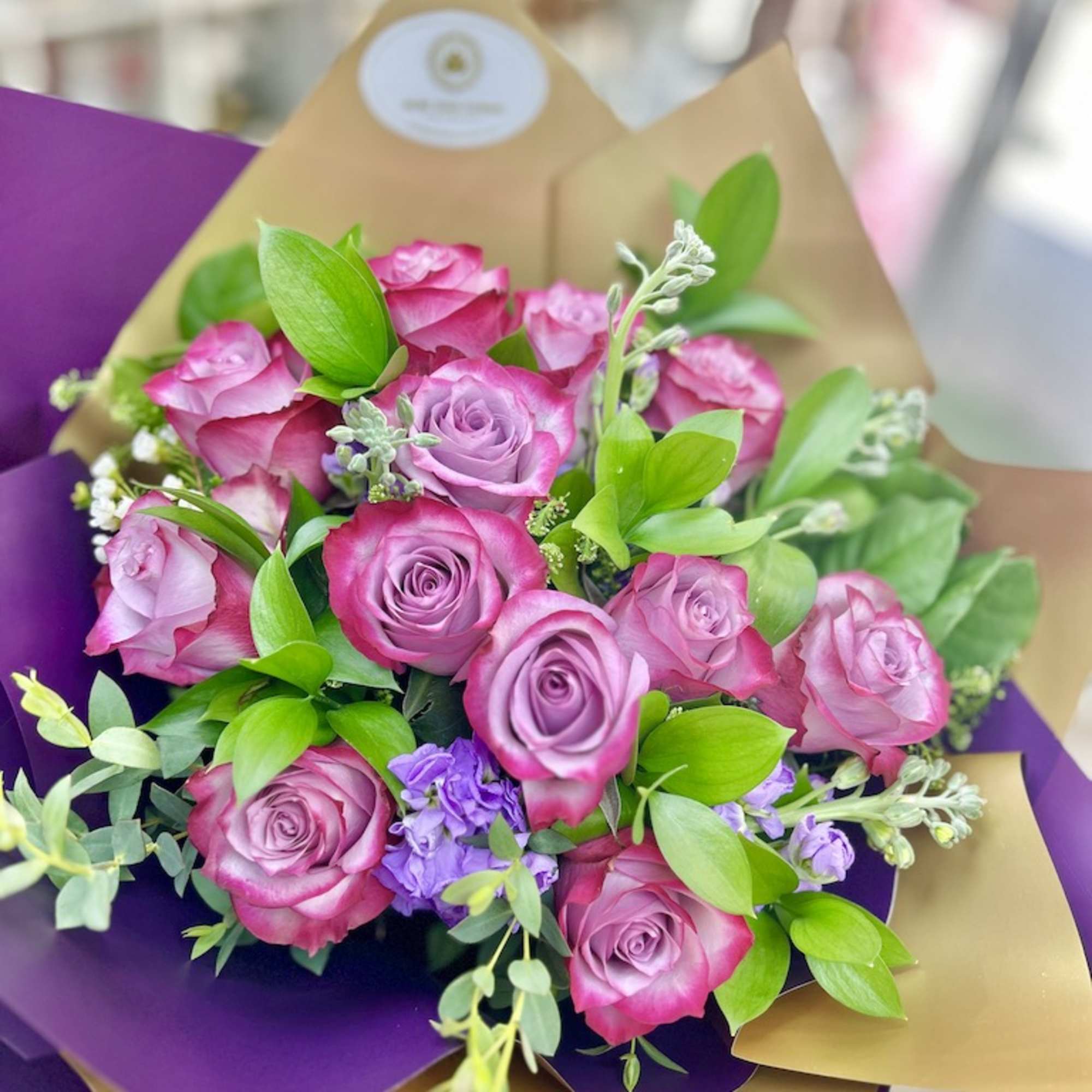 Hand-tied bouquet of pink and lavender roses wrapped in purple and gold paper