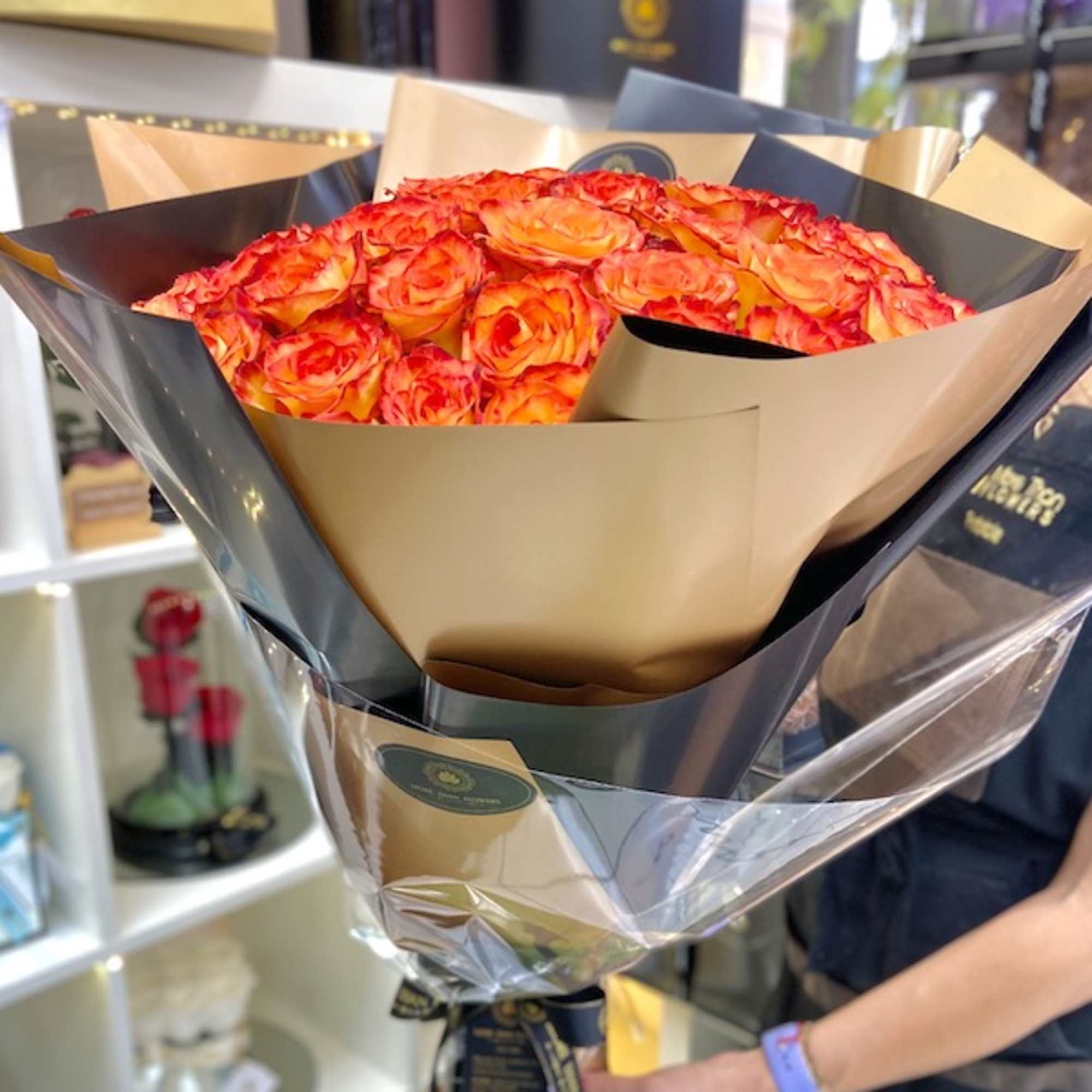 Large bouquet of orange and red roses wrapped in black and gold paper with clear cellophane and ribbon