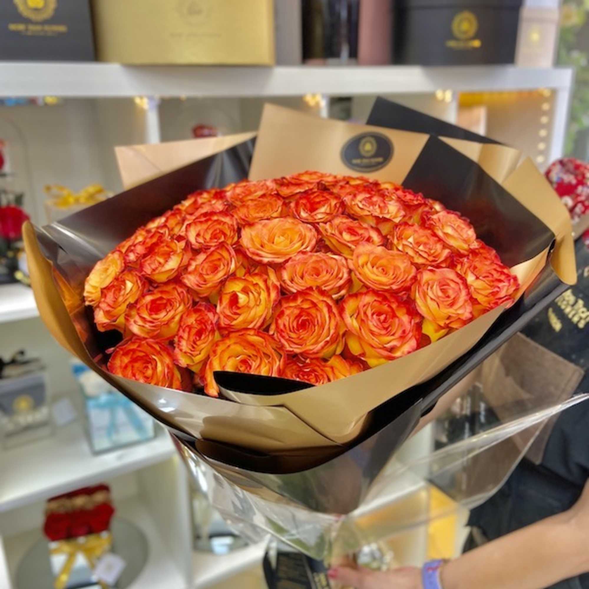 Bouquet of orange and red roses wrapped in black and gold paper held in a flower shop