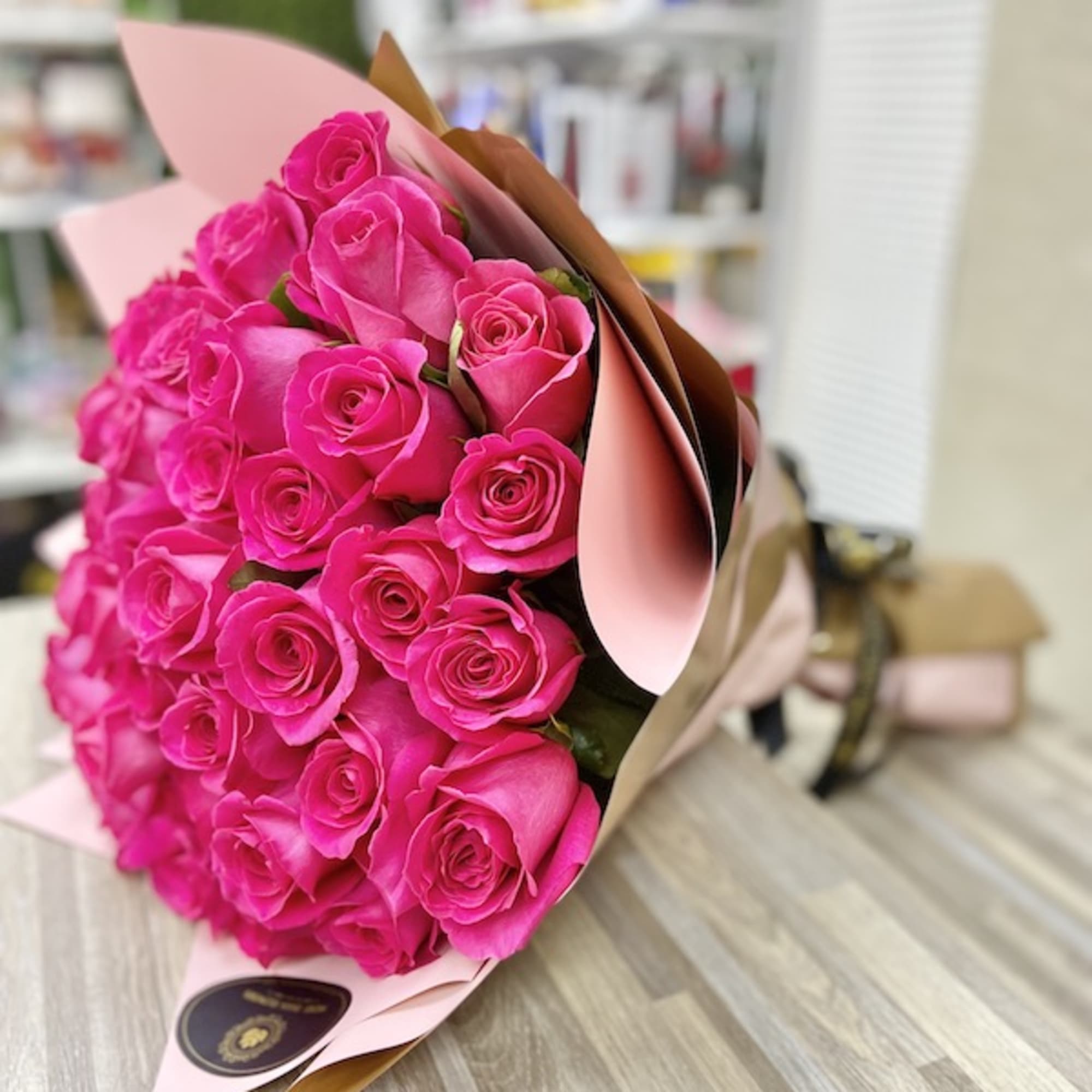 Bouquet of bright pink roses wrapped in pink and tan paper on a wood surface