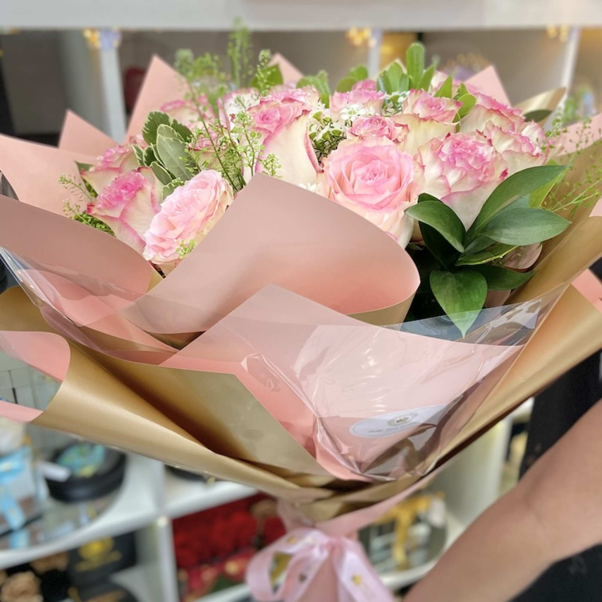 Handheld bouquet of pink and white roses wrapped in pink and gold paper.