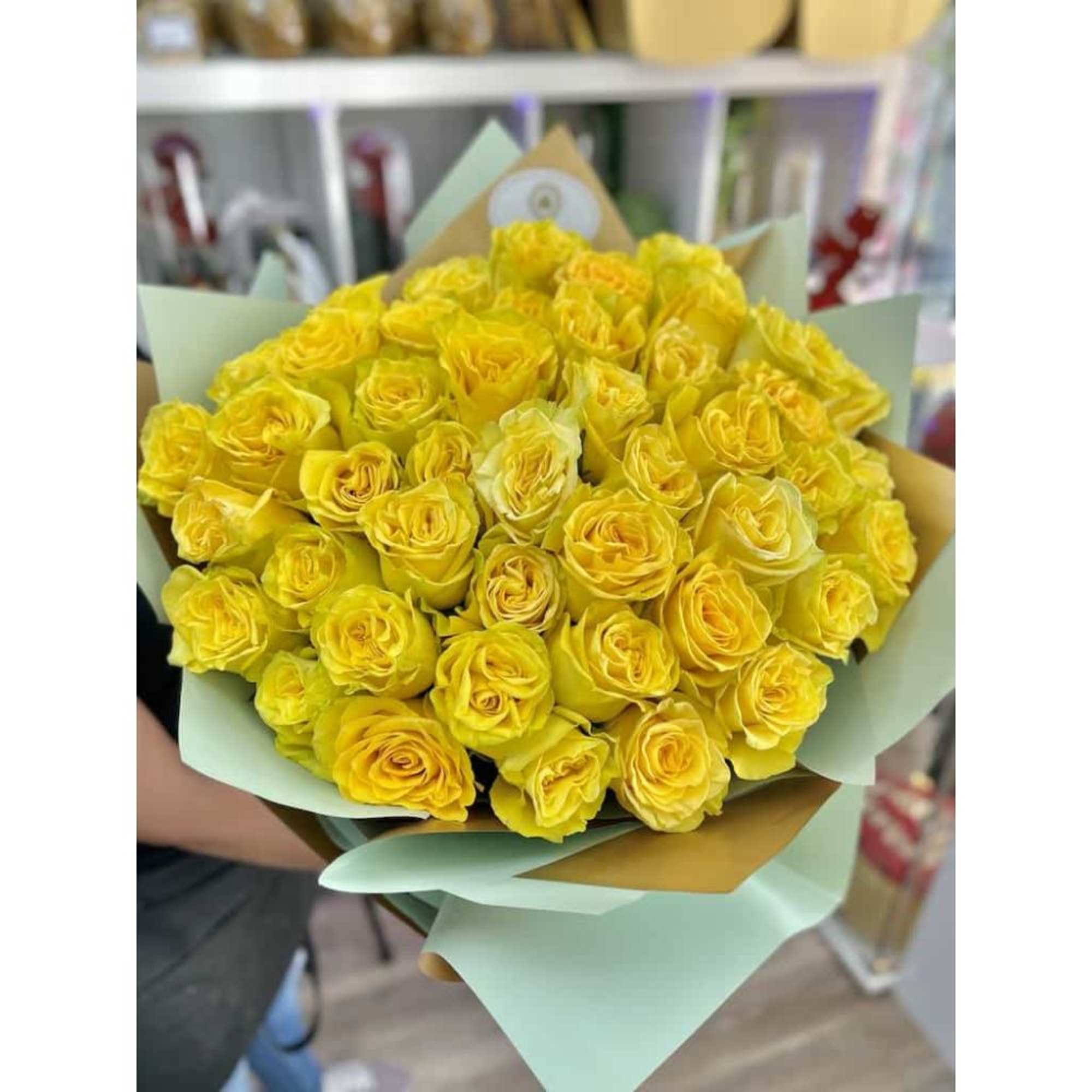 Large bouquet of bright yellow roses wrapped in pastel green and kraft paper
