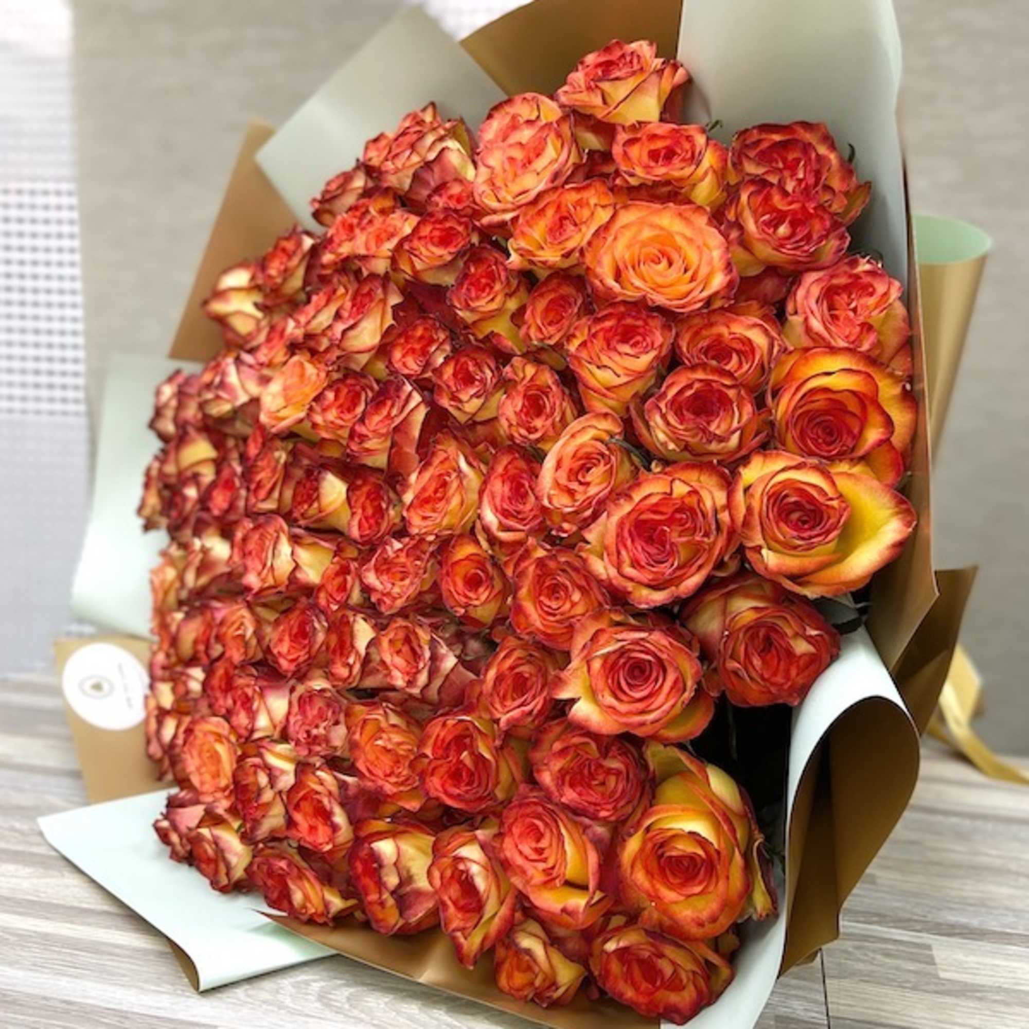 Large wrapped bouquet of tightly clustered orange and red roses on a wooden surface