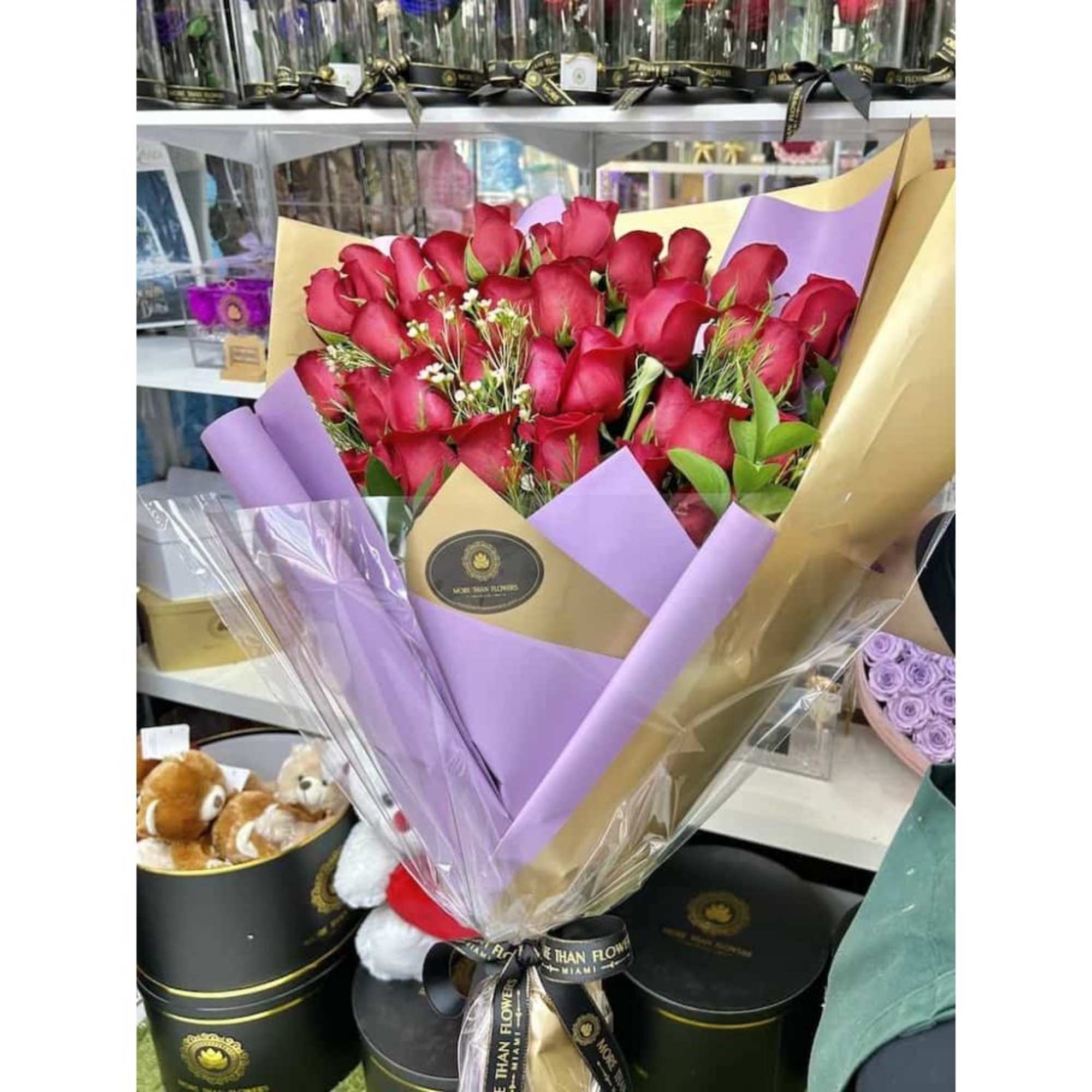 Large bouquet of red roses wrapped in lavender and tan paper with clear cellophane.