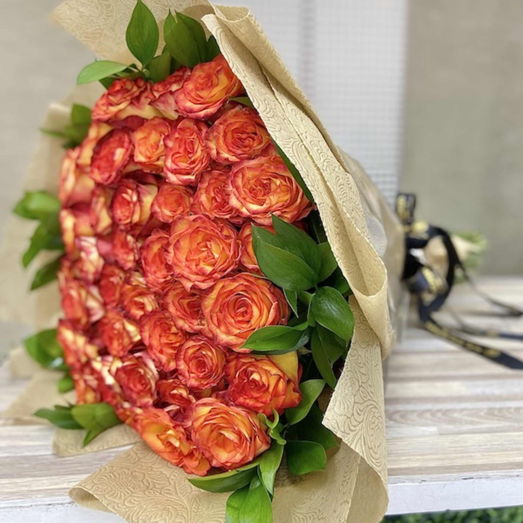Large bouquet of orange and red roses wrapped in embossed beige paper