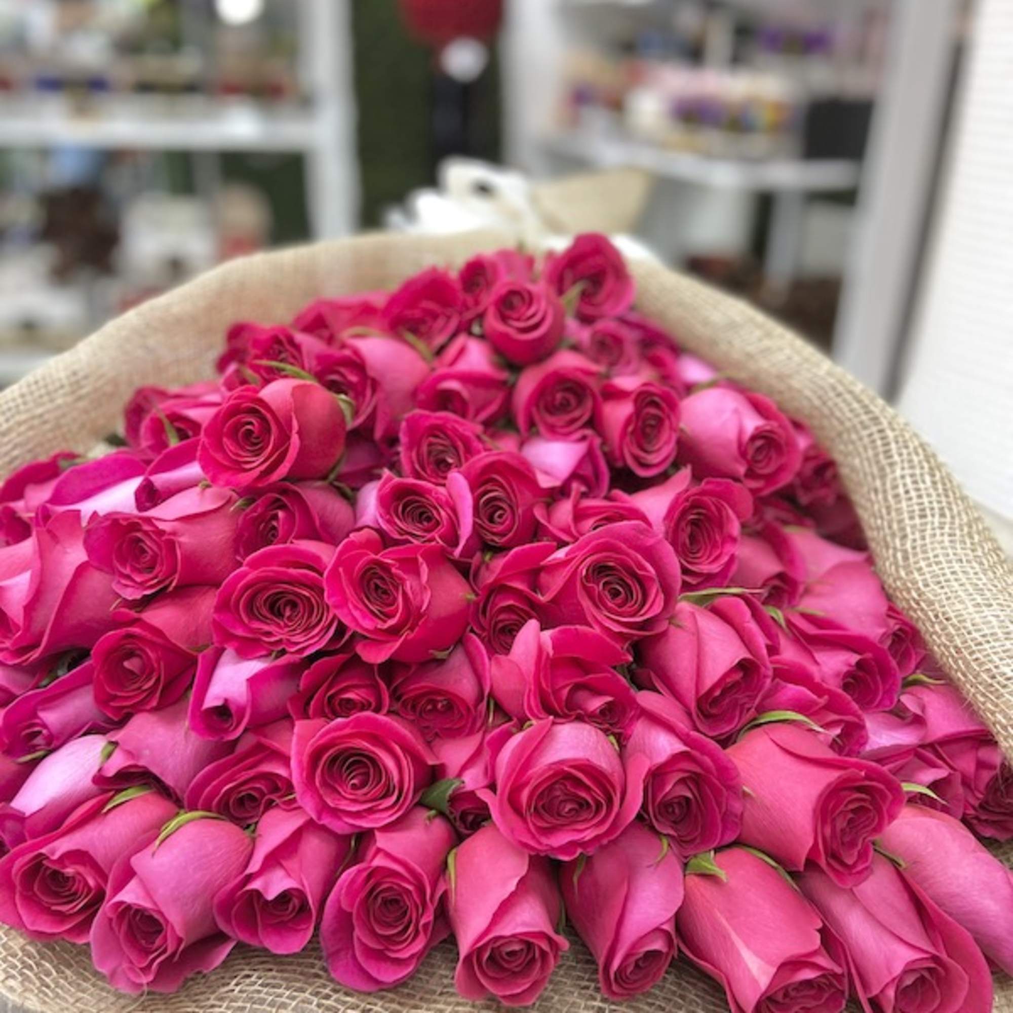Large bundle of bright pink roses wrapped in burlap on a light wood surface