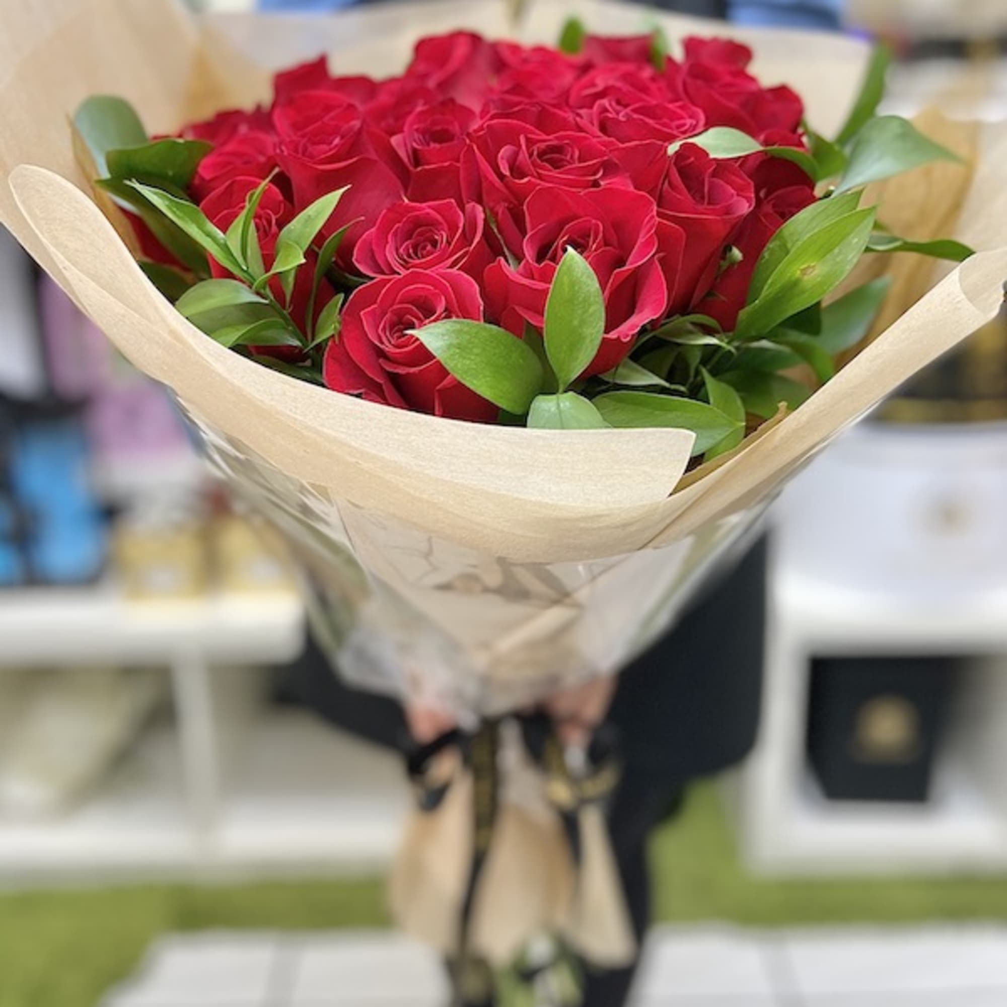 Handheld bouquet of red roses wrapped in kraft paper and cellophane