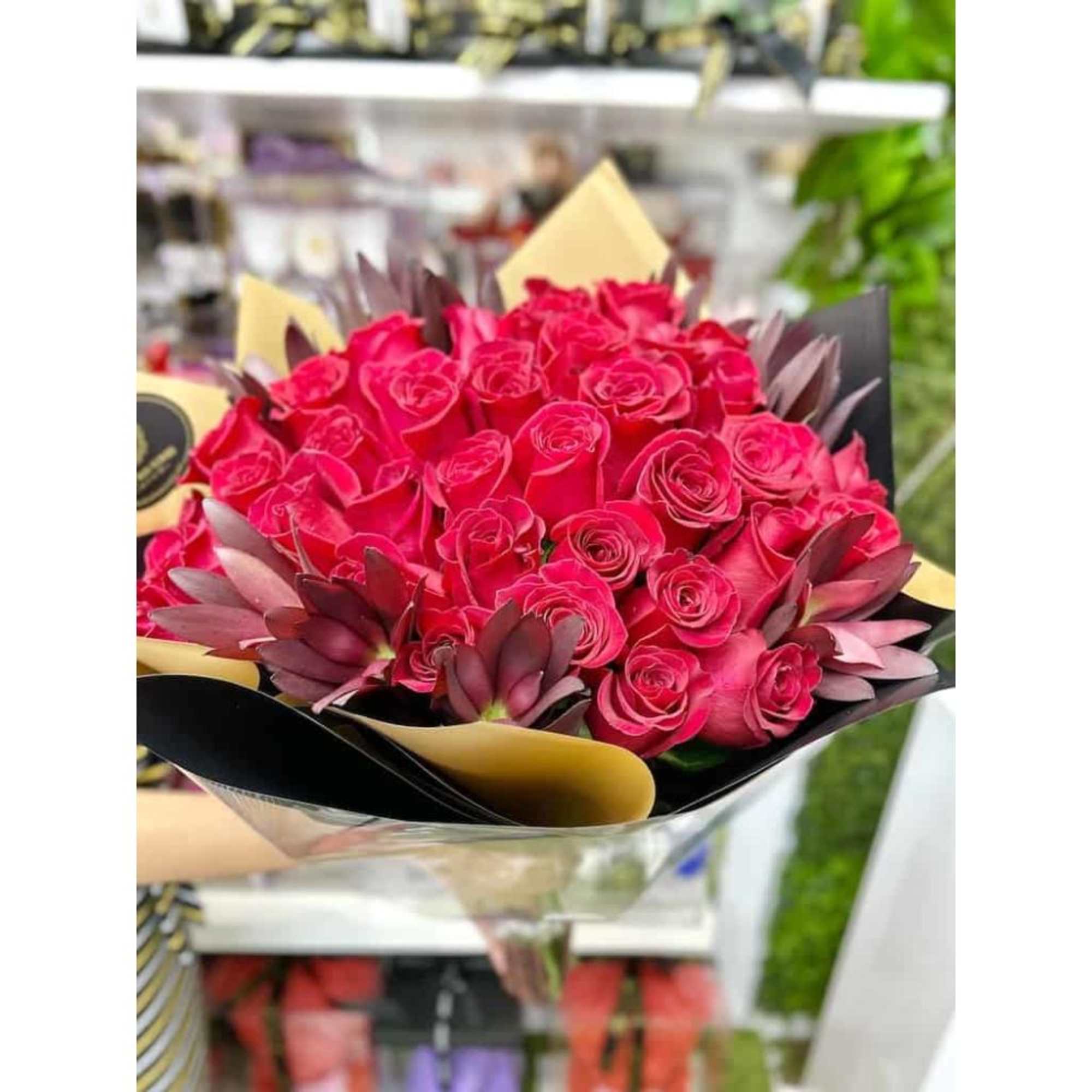 Large bouquet of bright pink roses with dark succulents wrapped in black and tan paper