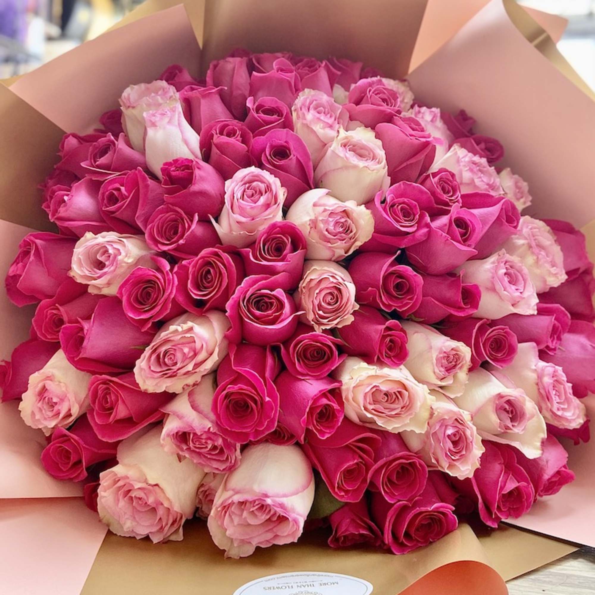 Large bouquet of hot pink and light pink roses wrapped in peach and gold paper