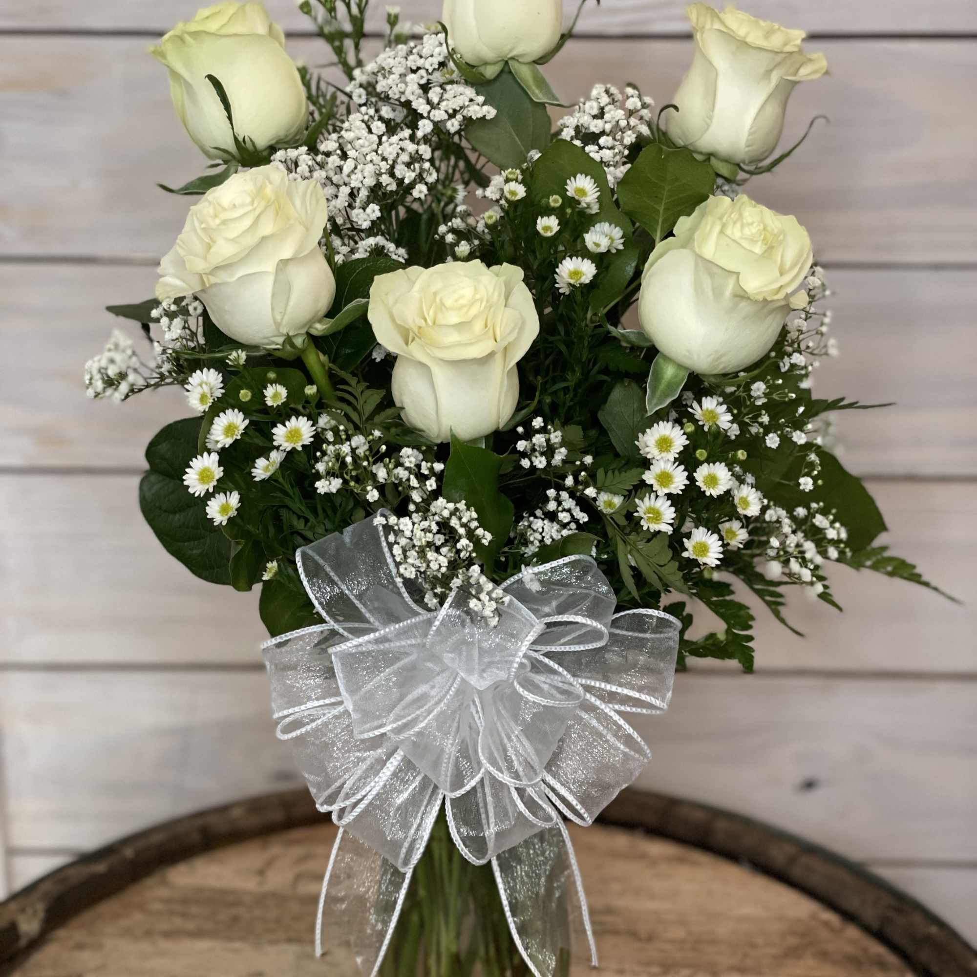 White roses in a glass vase with baby's breath and a sheer silver bow