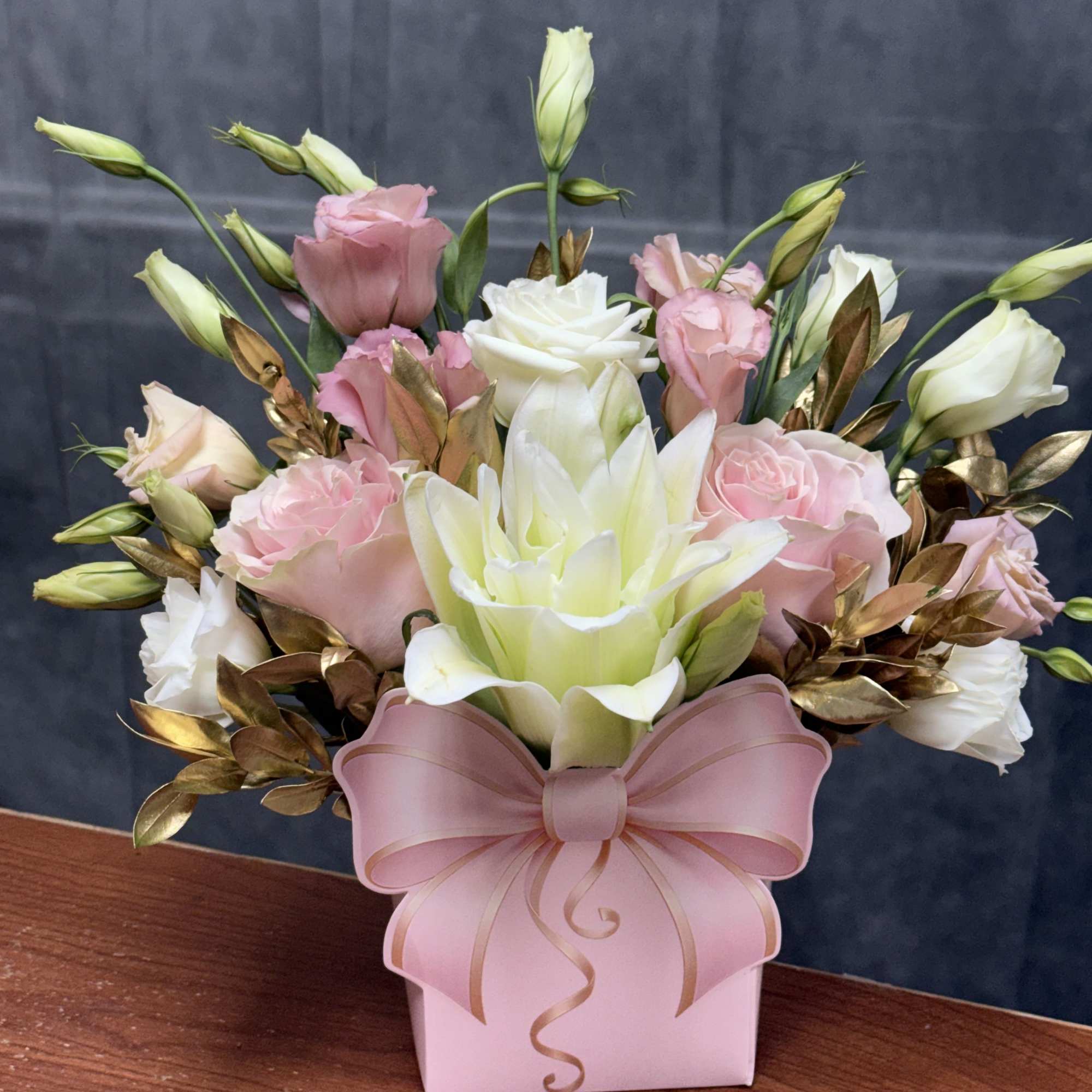 A luxurious arrangement featuring blush roses, white lilies, and golden foliage for